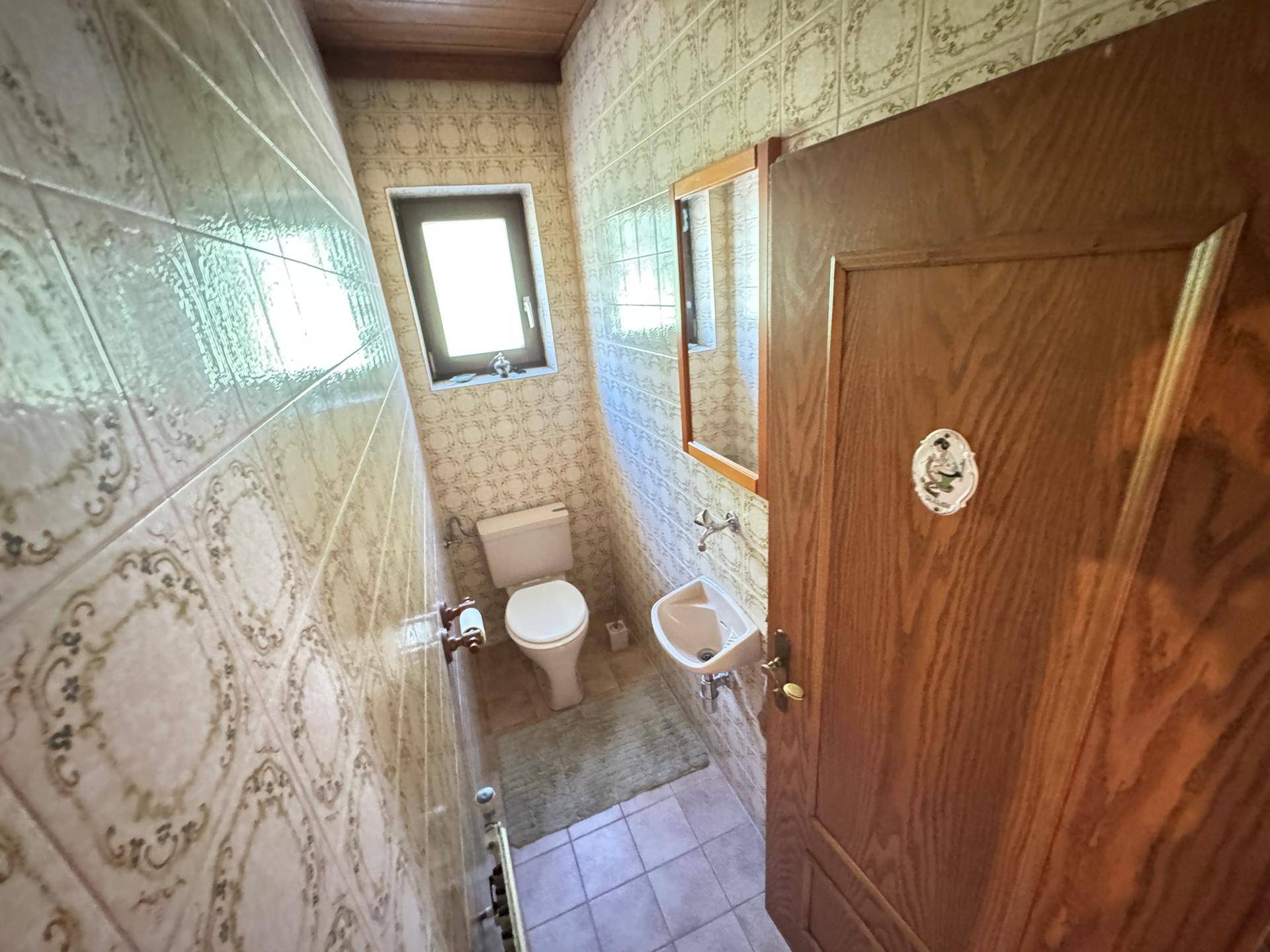Kleines Gäste-WC mit Fliesen an Wänden und Boden, Fenster, Toilette und einem Waschbecken.