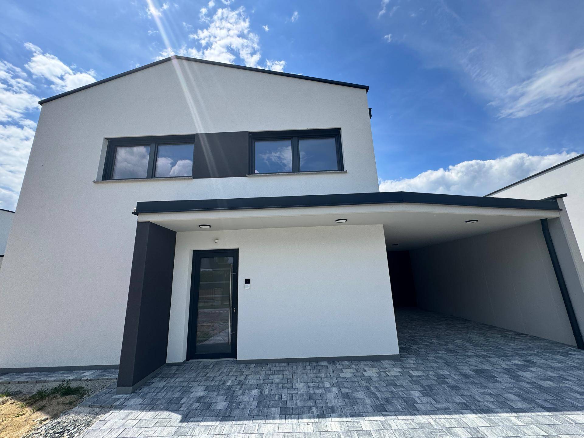 Vorderansicht des modernen Einfamilienhauses mit überdachtem Eingangsbereich und Carport.