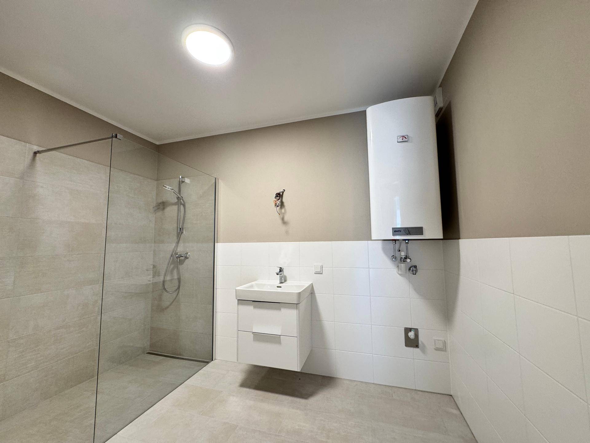 Badezimmer mit Dusche, Waschbecken und einem Warmwasserboiler an der Wand, praktisch eingerichtet.