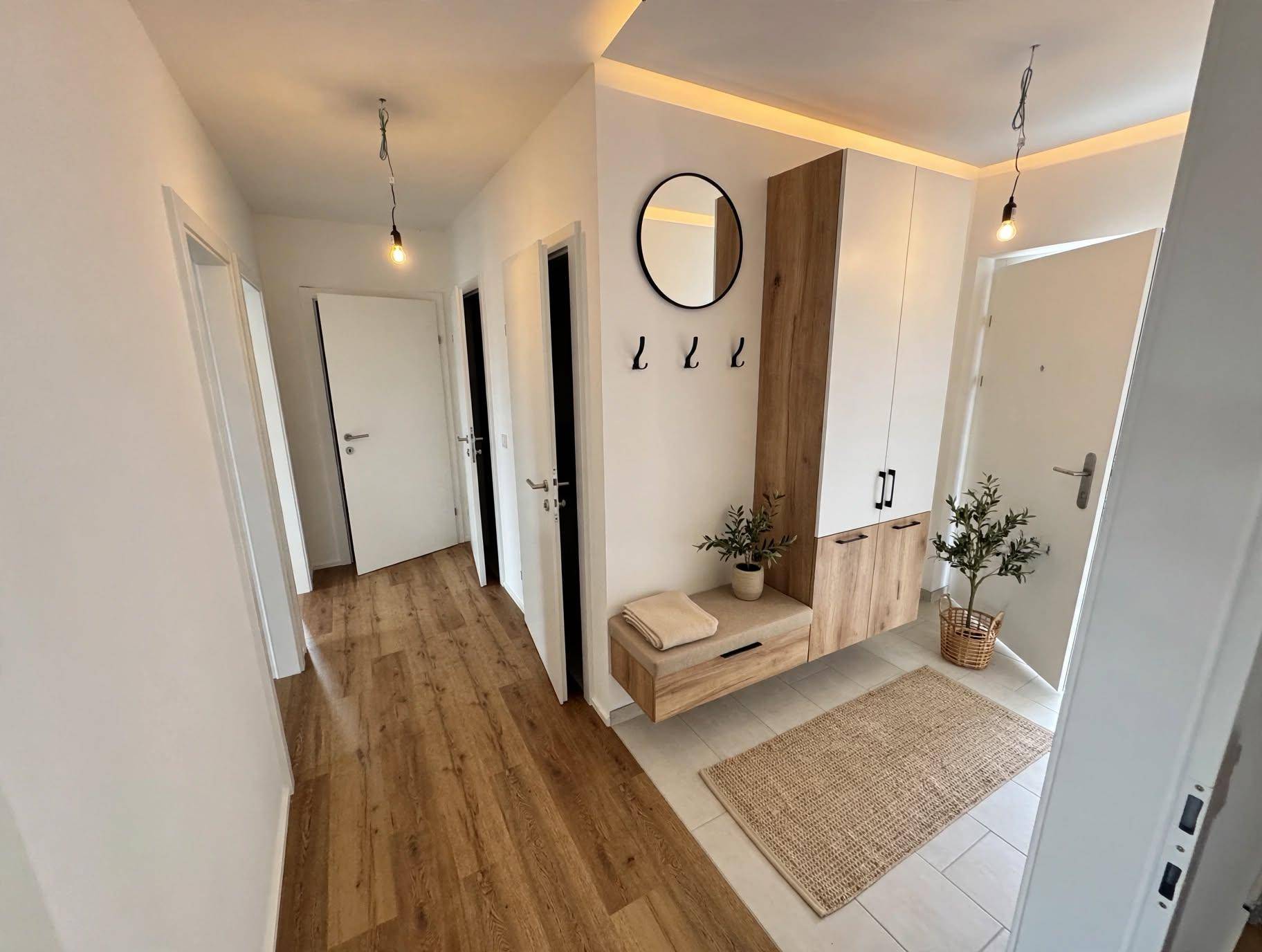 Heller Eingangsbereich mit modernem Garderobenschrank, Spiegel und Holzoptikboden.