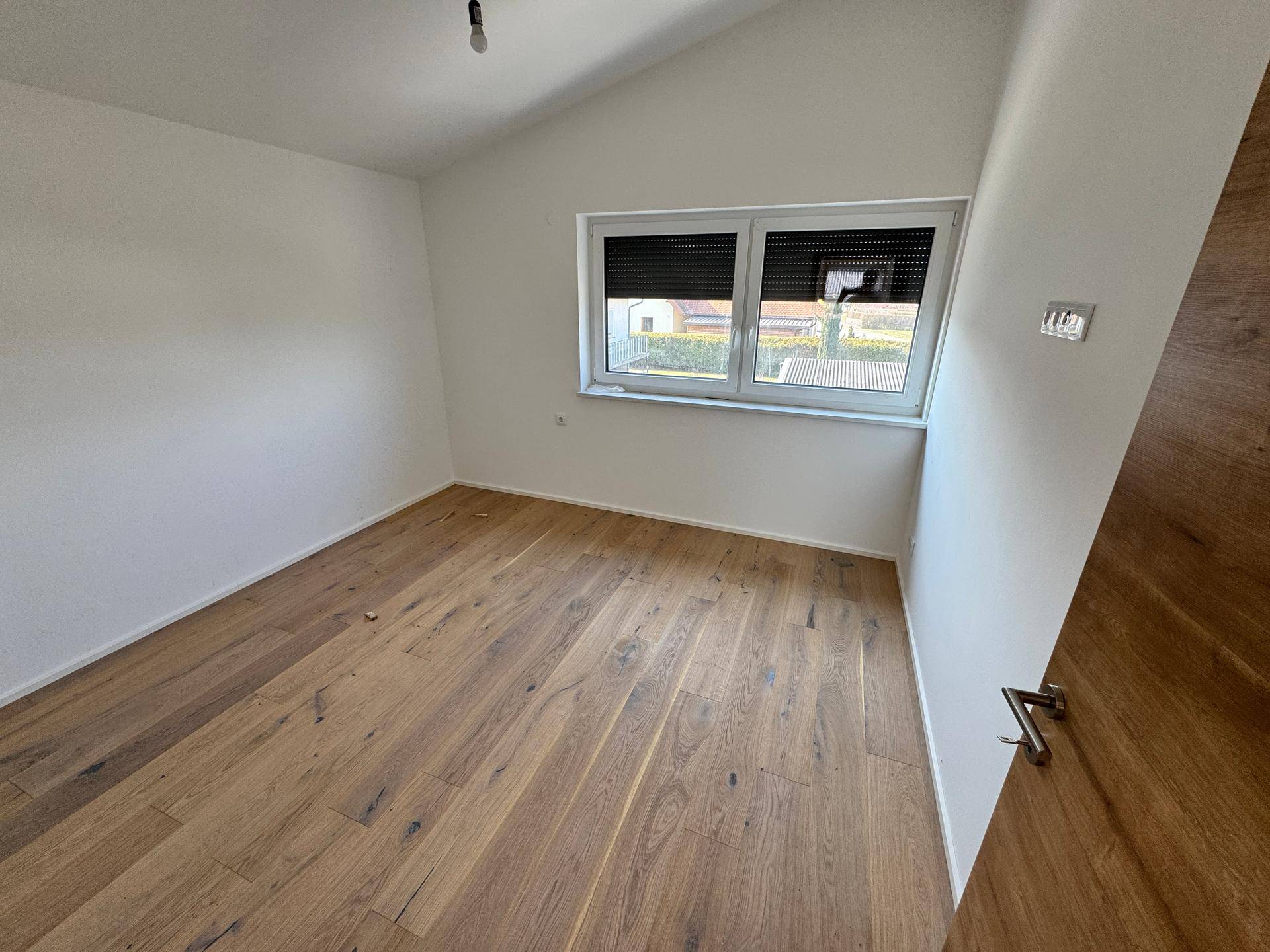 Heller Raum im Dachgeschoss mit Holzboden und einem Fenster, das den Blick nach draußen ermöglicht.