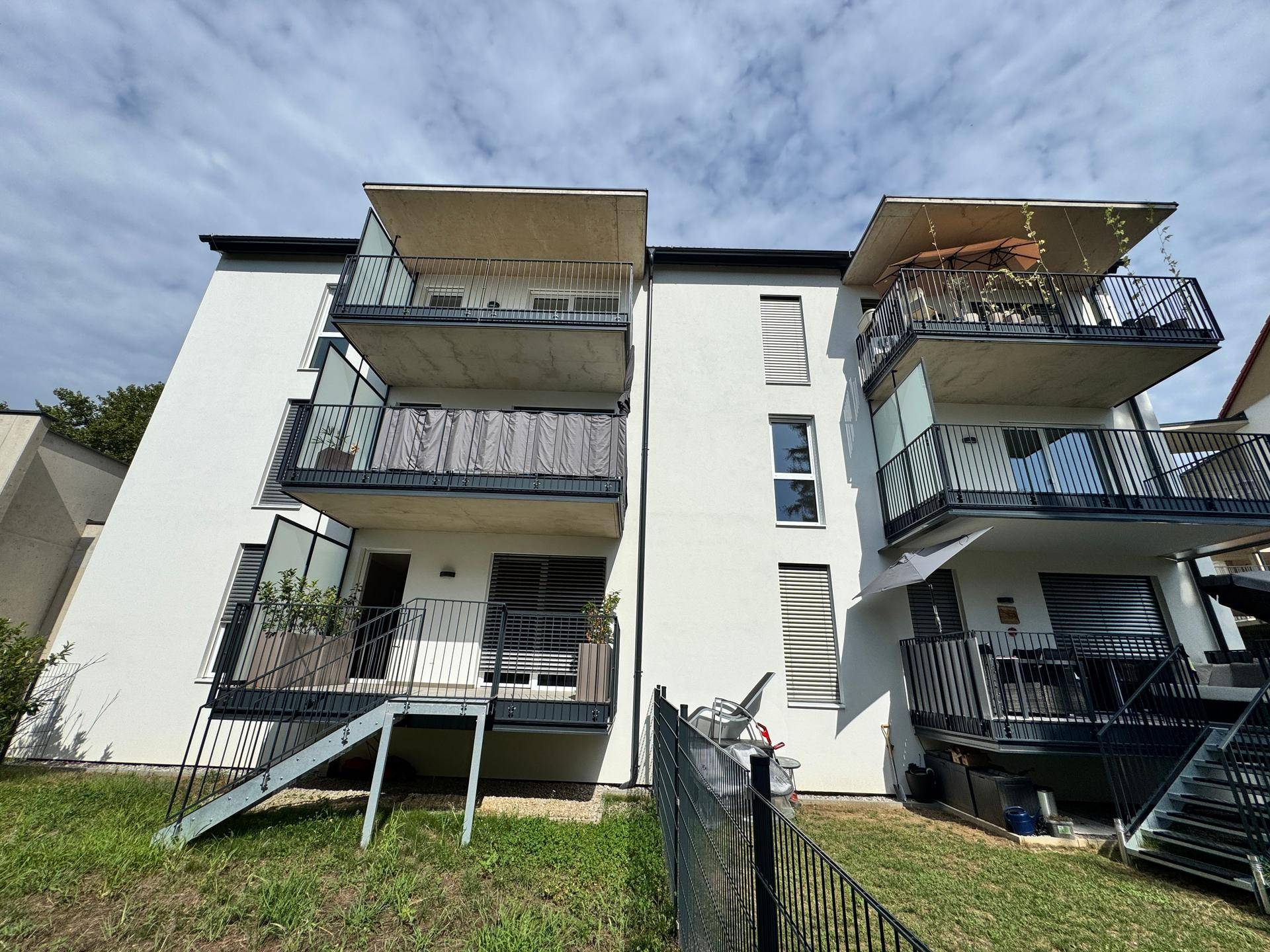 Fassade eines modernen Wohnhauses mit mehreren Balkonen und Zugang zum Gartenbereich.