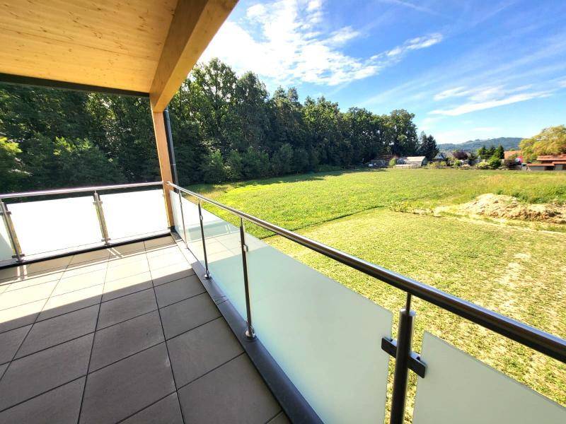 Überdachter Balkon mit Fliesenboden, Glasgeländer und weitem Blick ins Grüne.