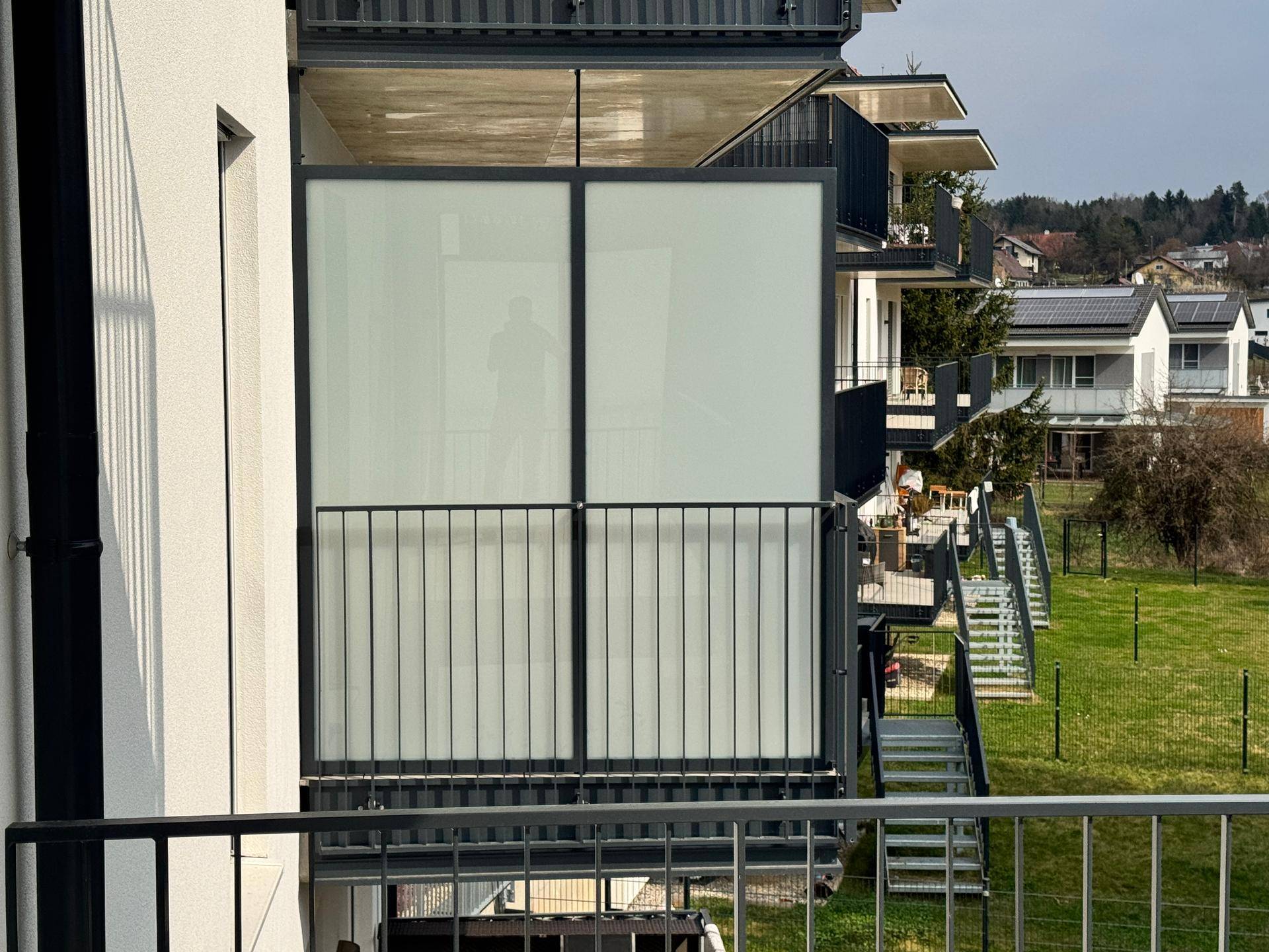 Moderner Balkon mit Milchglas-Sichtschutz und Blick auf die grüne Umgebung und weitere Balkone.