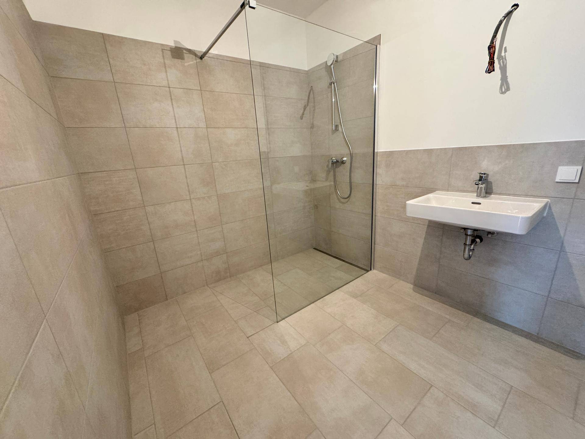 Modernes Badezimmer mit großer Glasdusche und Waschbecken, ausgestattet mit hellen Fliesen.