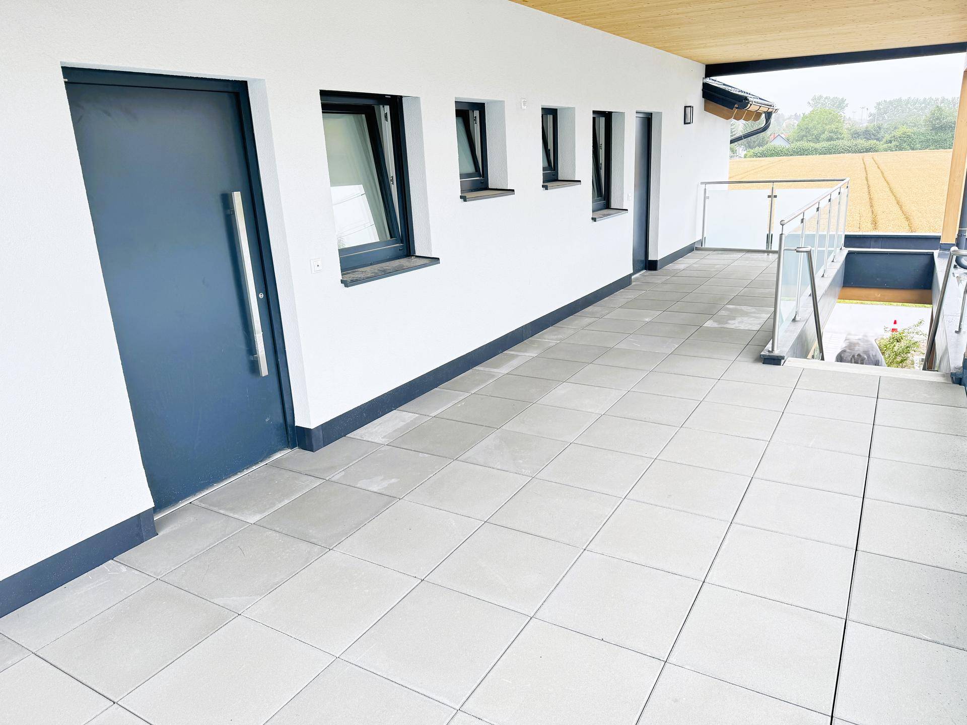 Überdachte Terrasse mit Fliesenboden und Zugang zum Eingangsbereich des Gebäudes.