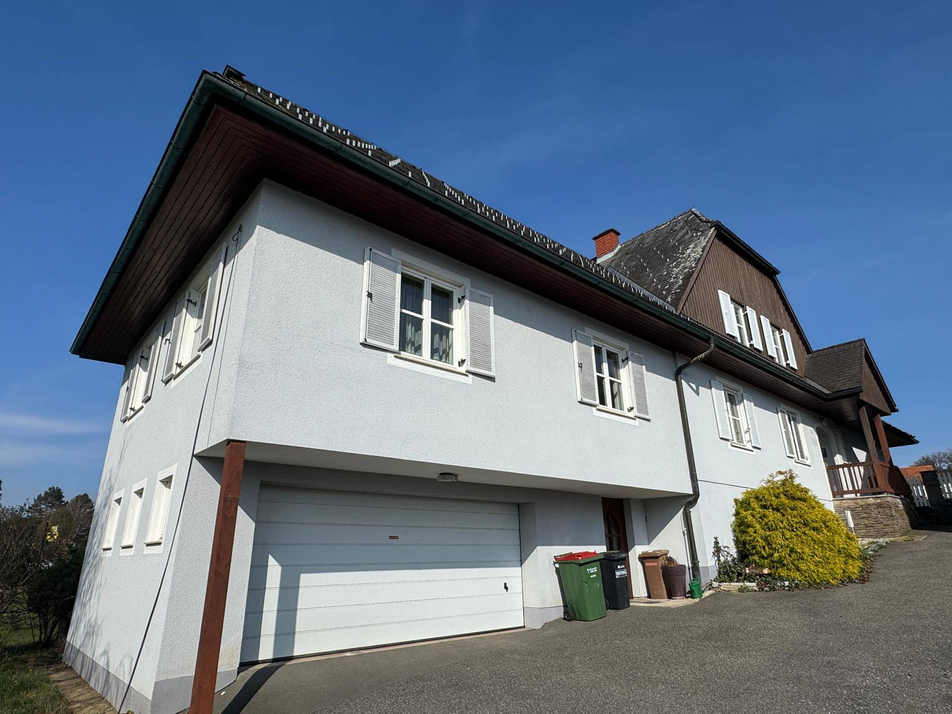 Seitenansicht des Hauses mit weißer Fassade und einer großen Garage im Erdgeschoss.