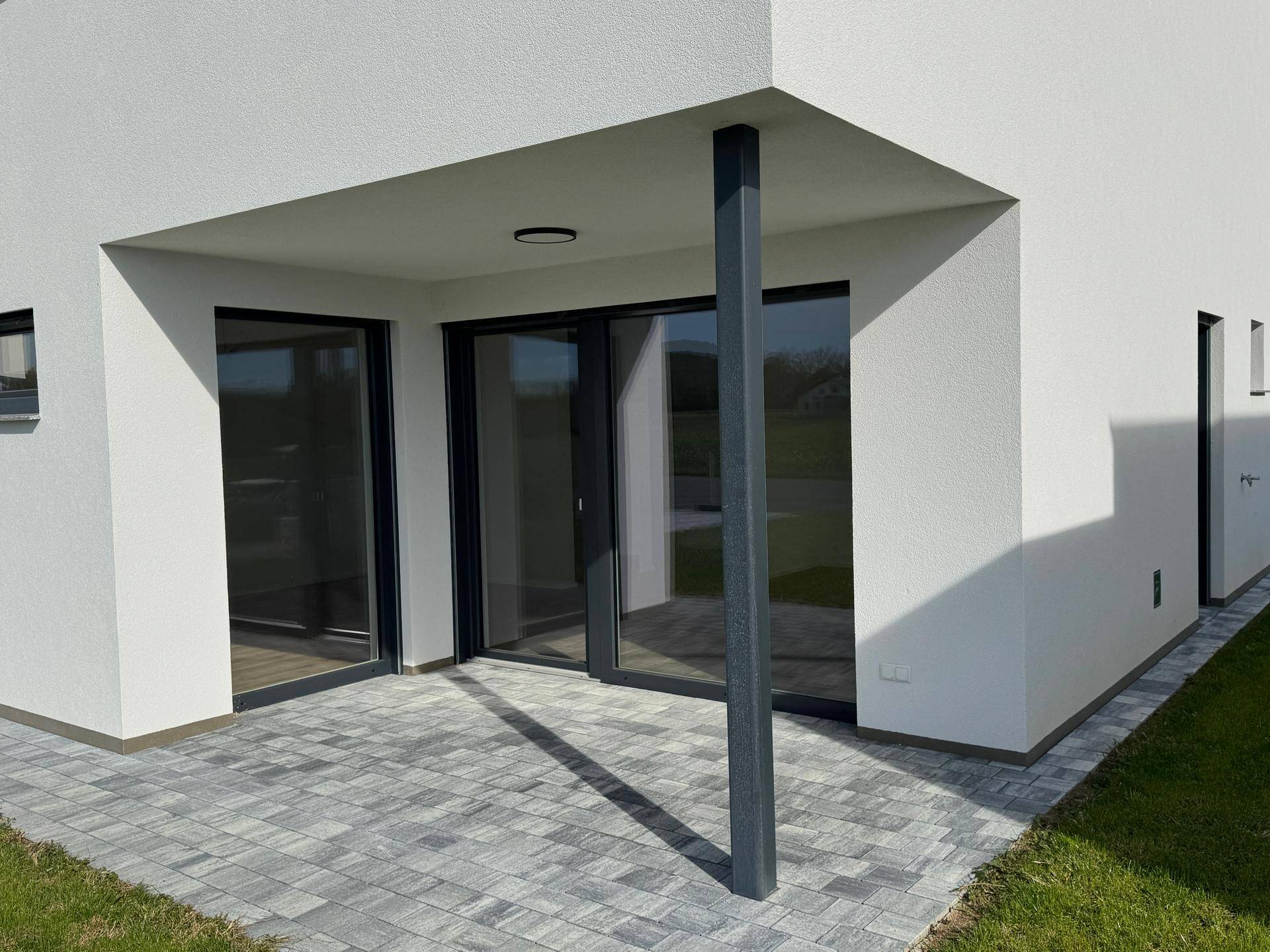 Großzügige Terrasse mit Schiebetüren, gepflastertem Boden und angrenzender Rasenfläche.