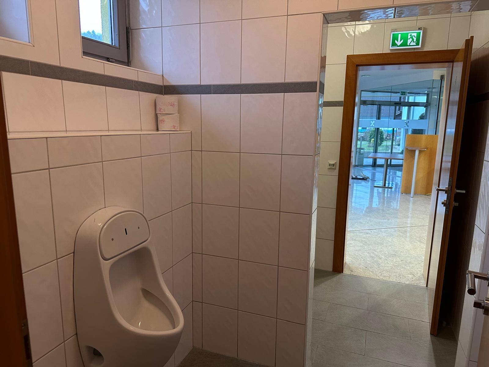 WC-Raum mit Fliesen, Urinal und Fenster für natürliche Belüftung.
