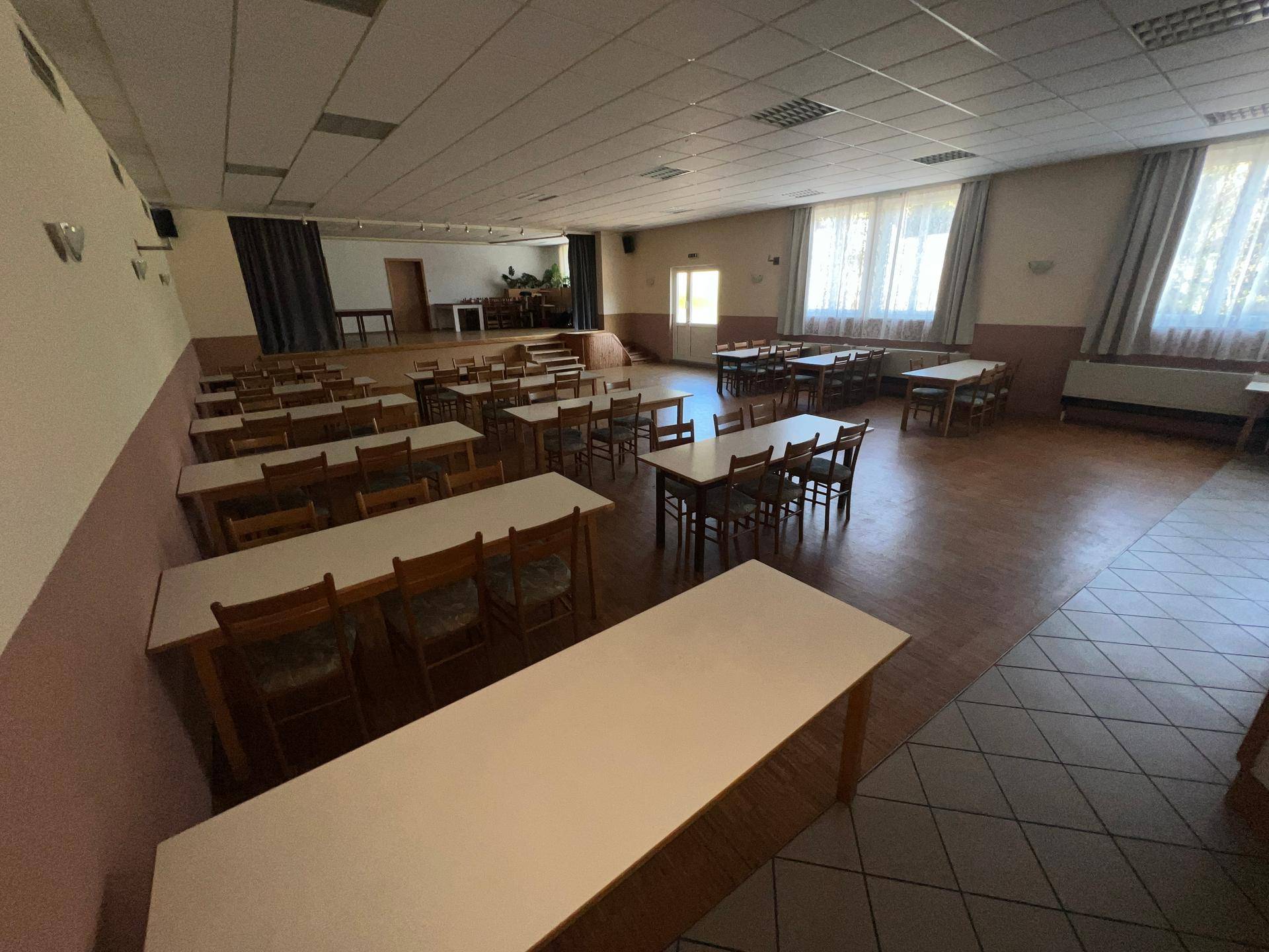 Großer Veranstaltungssaal mit Holzboden, vielen Tischen und Stühlen sowie einer Bühne.