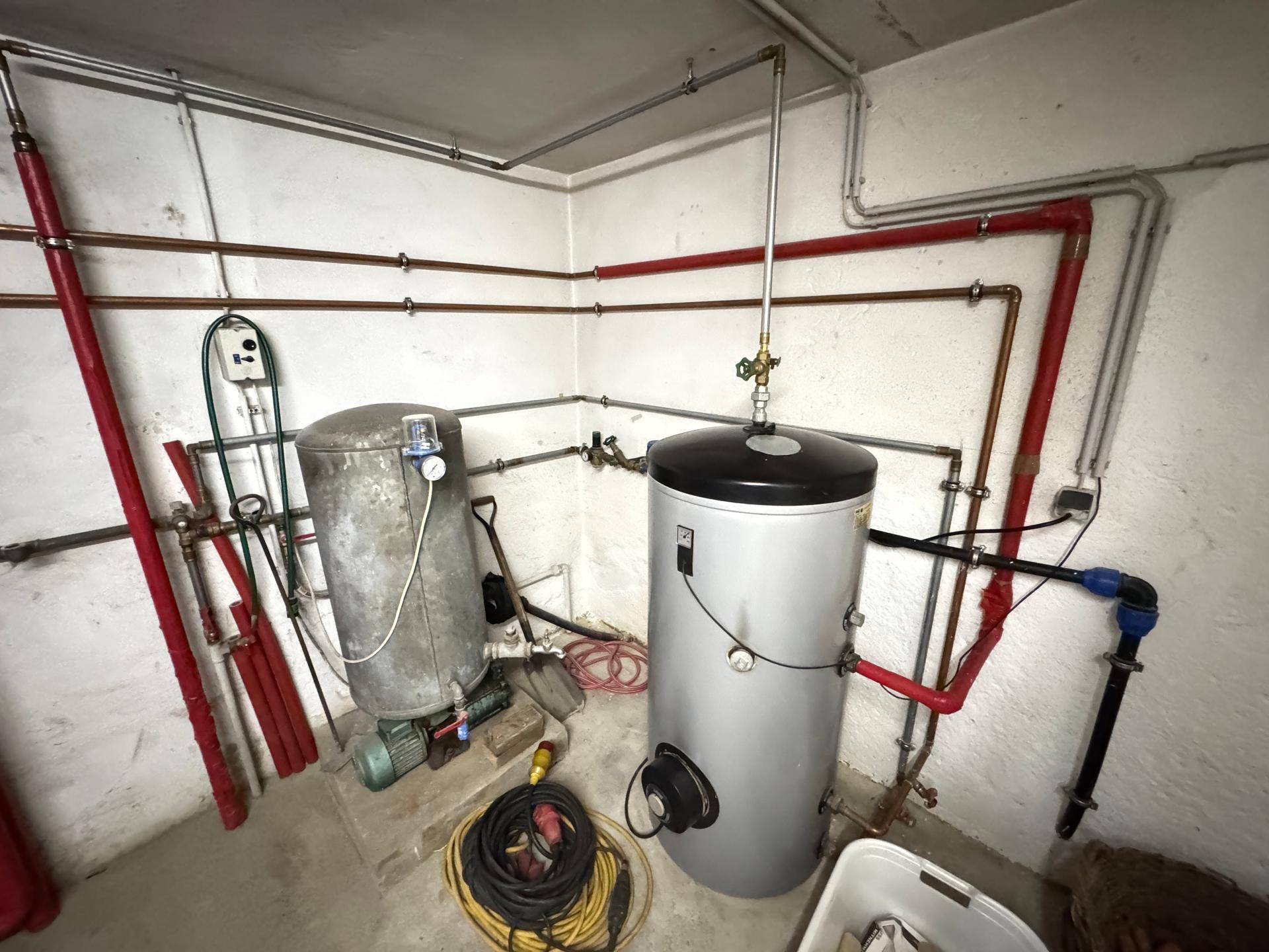 Kellerraum mit zwei Warmwasserspeichern und sichtbaren Rohrleitungen für die Wasserversorgung.