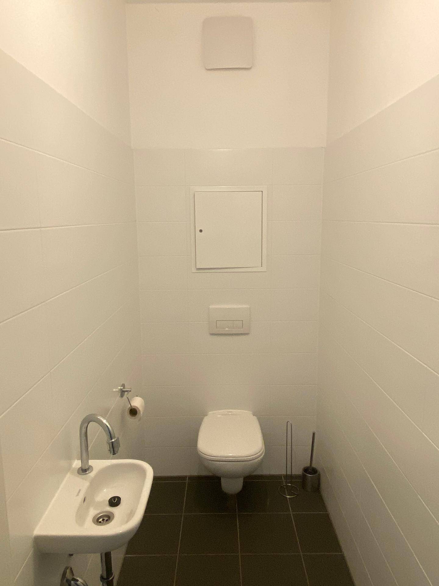 Kleines Gäste-WC mit wandhängender Toilette, Handwaschbecken und weißen Fliesen.