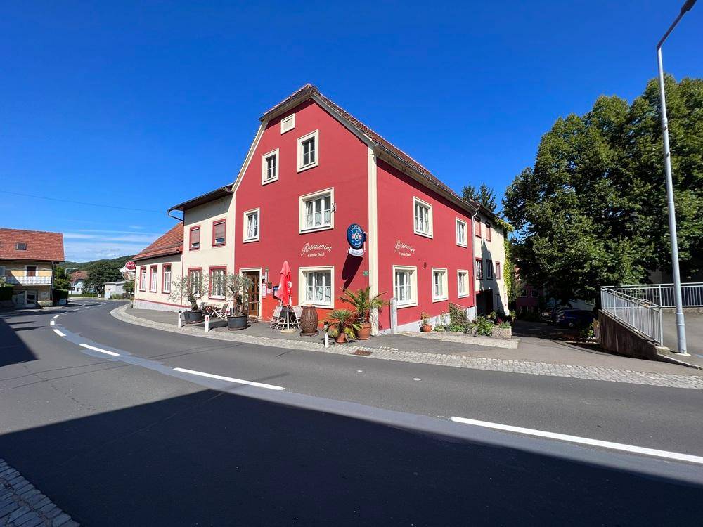 Rotes Gebäude mit weißen Fenstern und Restaurant an einer Straßenecke unter blauem Himmel.