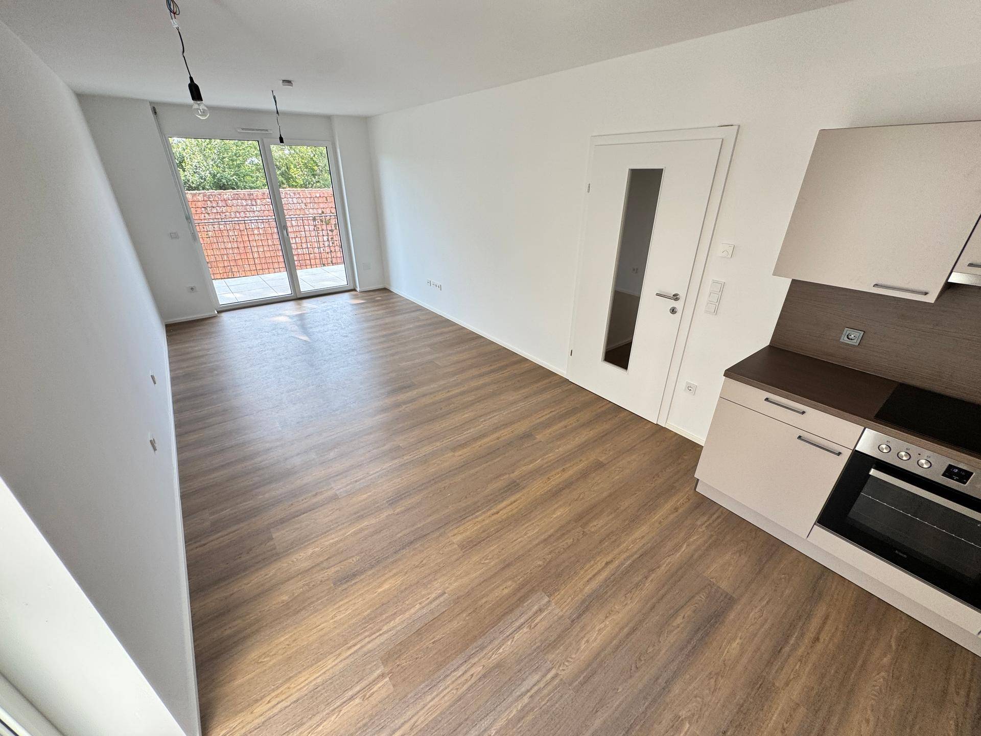 Offener Wohnbereich mit integrierter Küchenzeile und Zugang zu einem sonnigen Balkon.