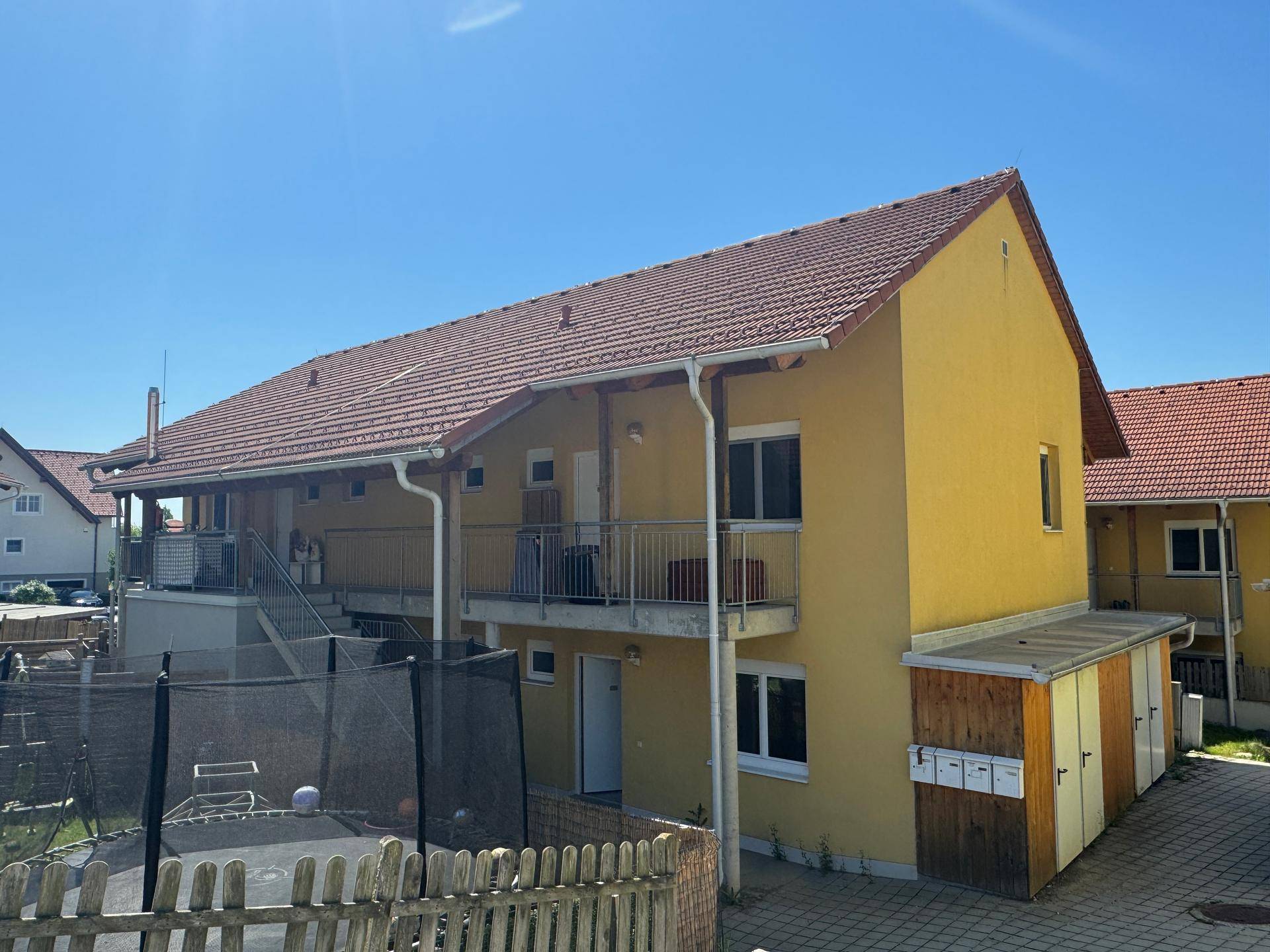 Gelbes Mehrfamilienhaus mit Balkonen, Außentreppe und Trampolin im Gartenbereich.