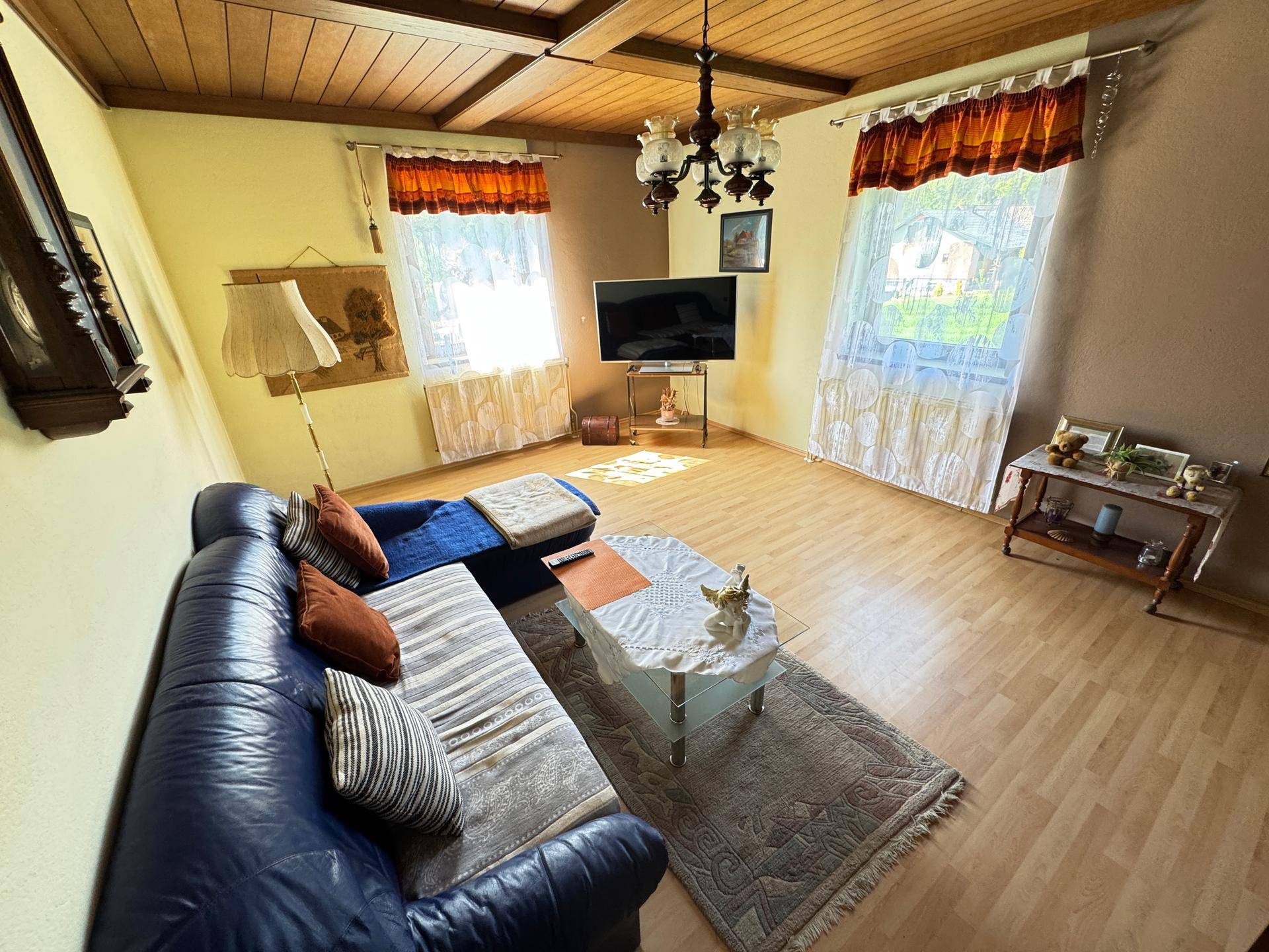 Gemütliches Wohnzimmer mit Holzbalkendecke, Ledersofa, Couchtisch und einem Fernseher.