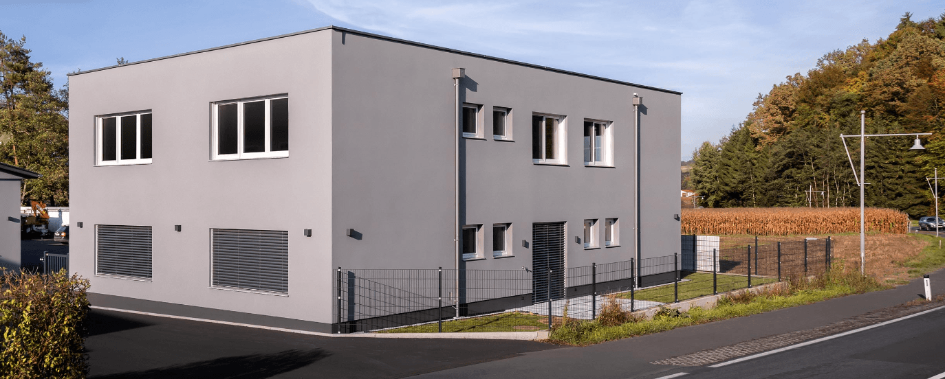 Ansicht des modernen Bürogebäudes von der Seite mit angrenzendem Feld und Wald im Hintergrund.