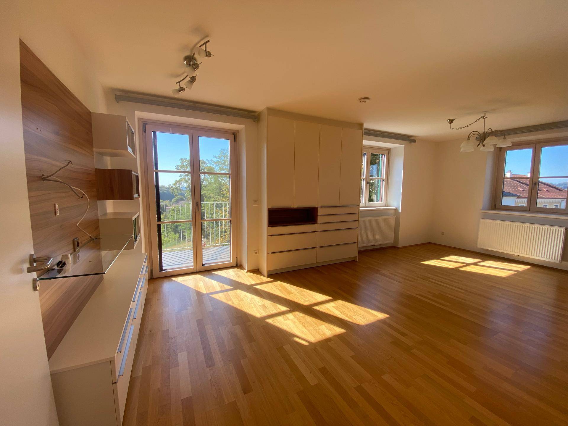 Lichtdurchflutetes Wohnzimmer mit Holzboden, Balkonzugang und weitem Blick ins Grüne.