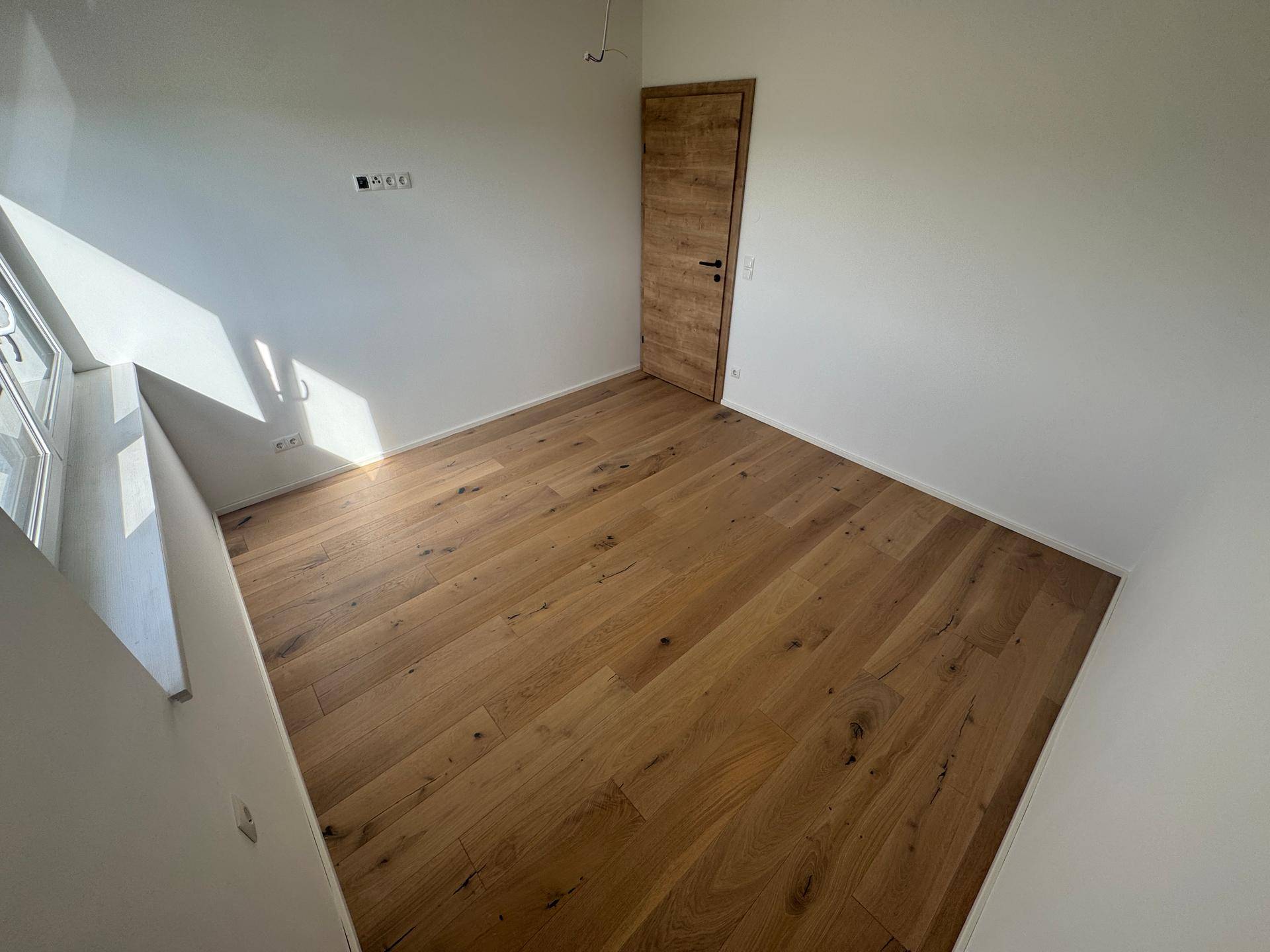 Schlafzimmer mit hellem Eichenparkett, weißen Wänden und Fenster.