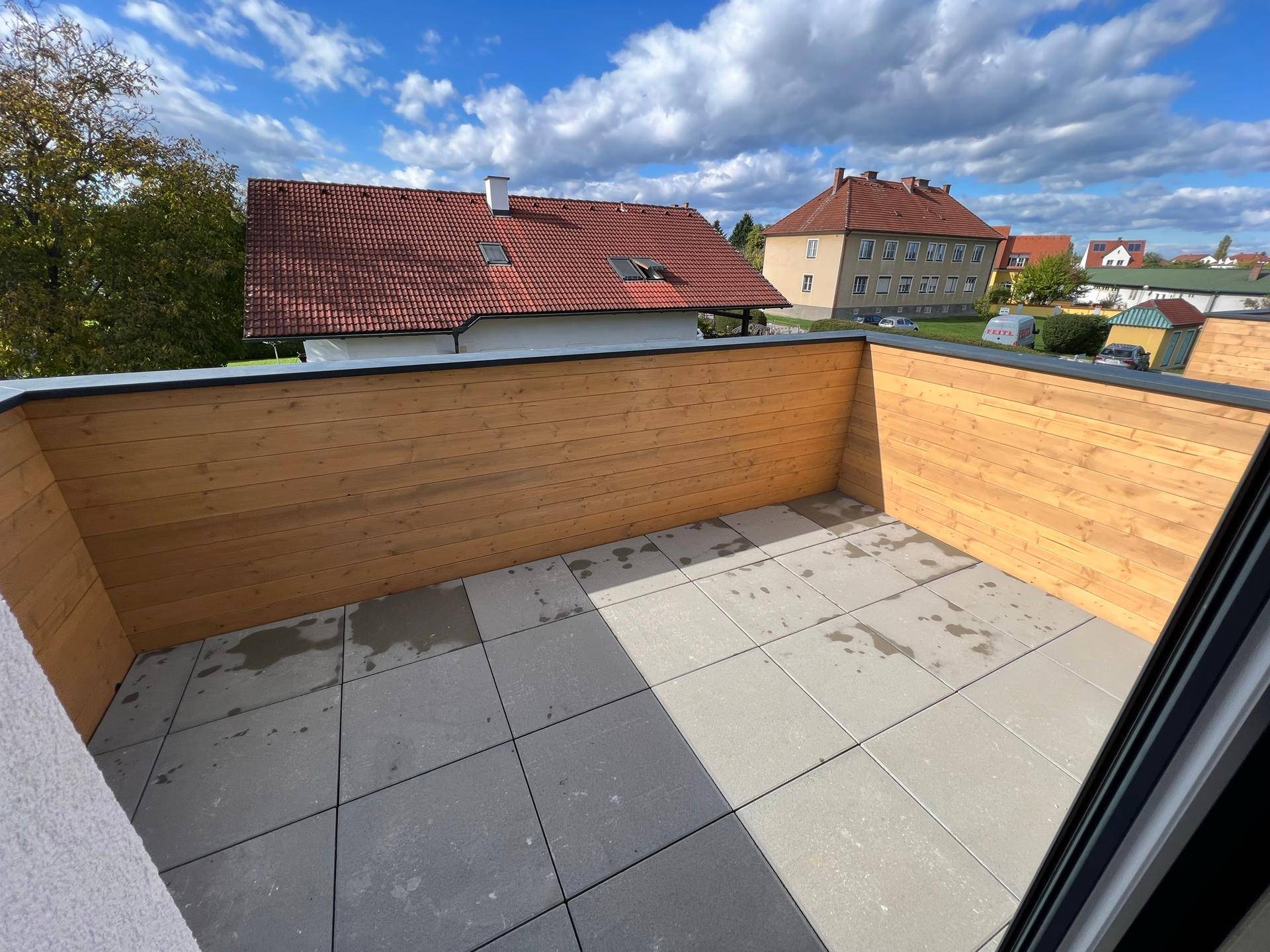 Geräumiger Balkon mit Holzwänden und Fliesenboden unter einem blauen Himmel, ideal für Entspannung.