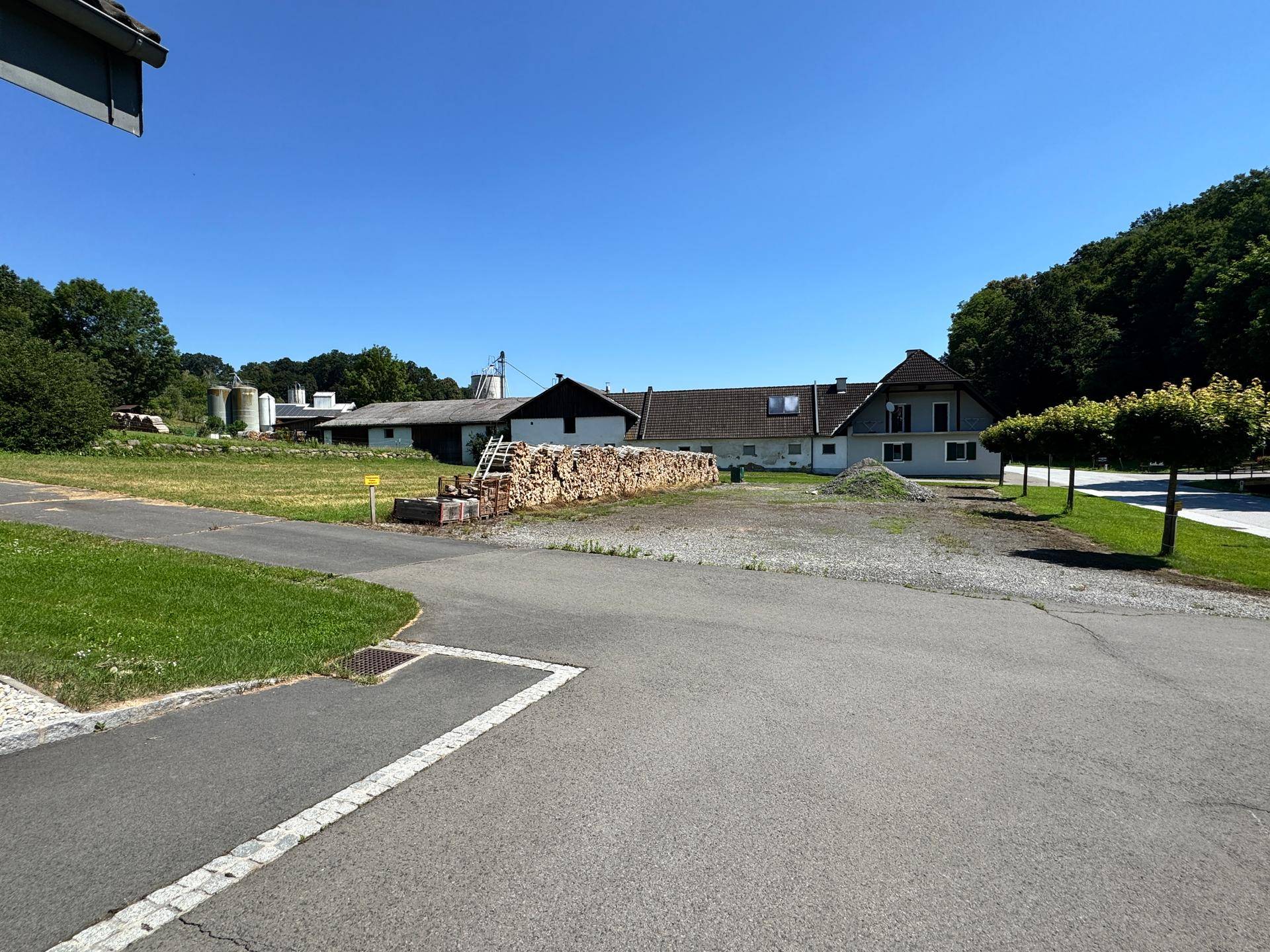 Übersicht über ein großes Grundstück mit mehreren Gebäuden, Holzstapeln und viel Grünfläche.