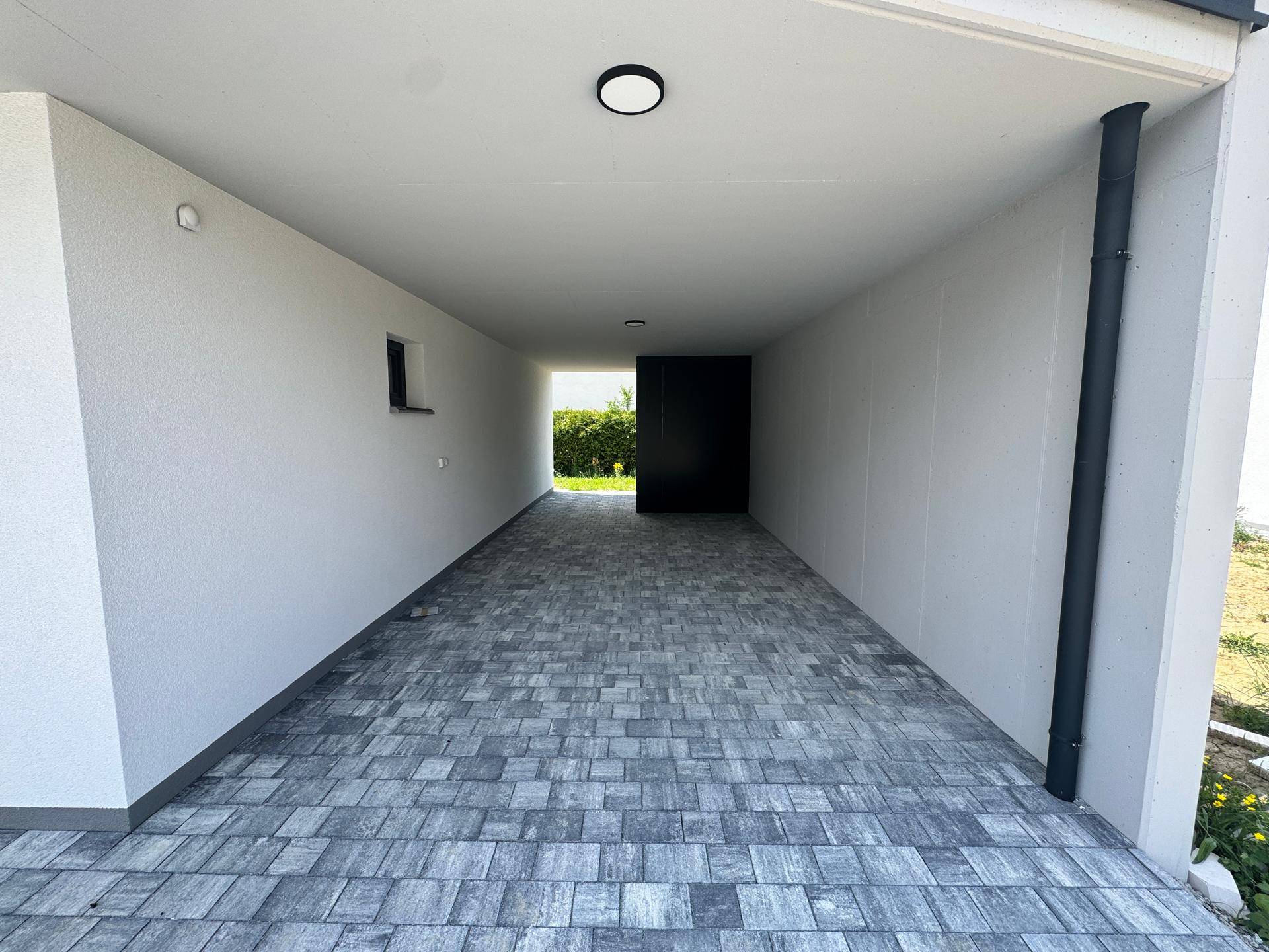 Geräumiger Carport mit gepflastertem Boden und weiß gestrichenen Wänden.