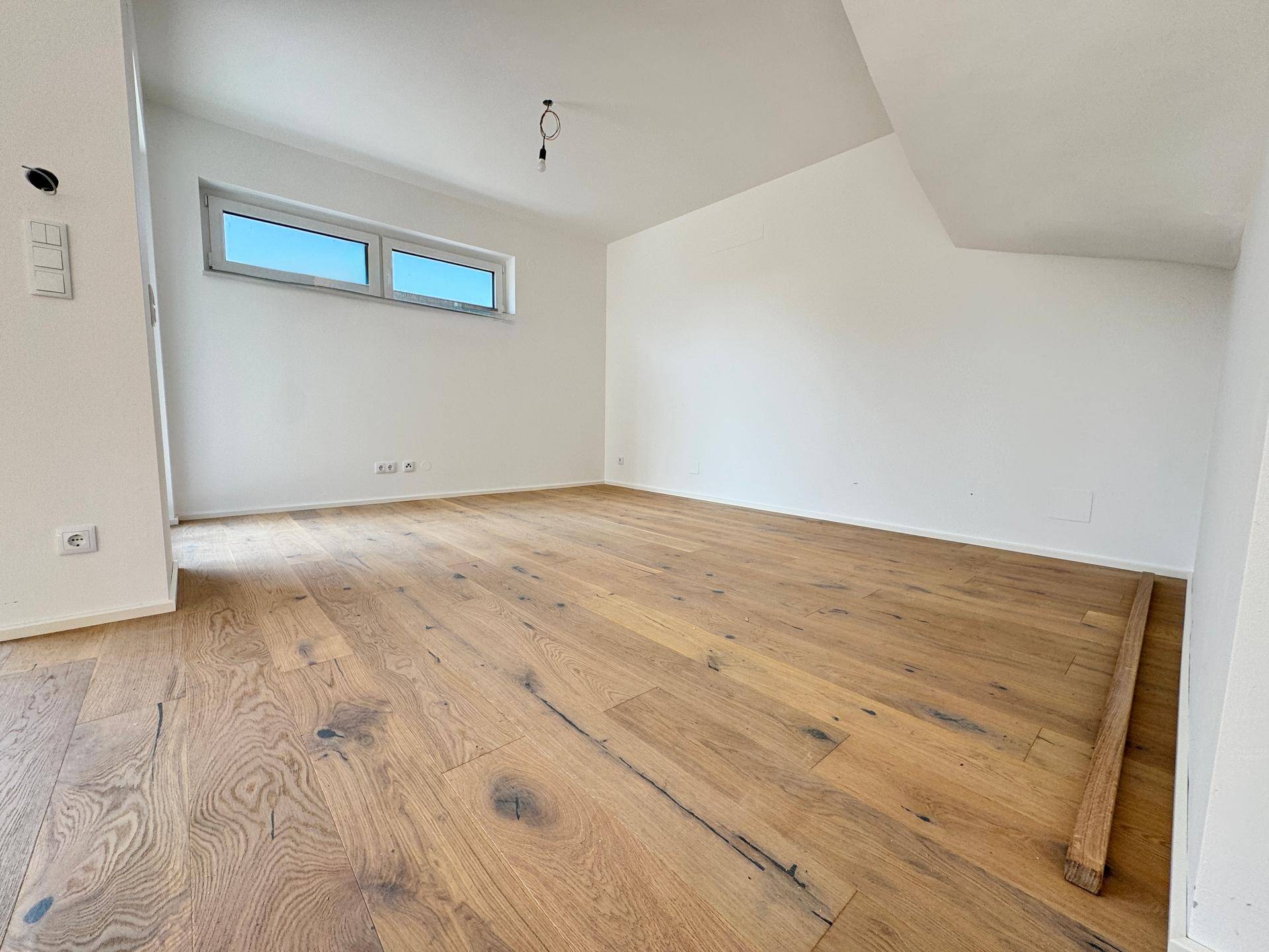 Heller Raum mit Holzboden und einem Fenster, das viel Tageslicht hereinlässt.