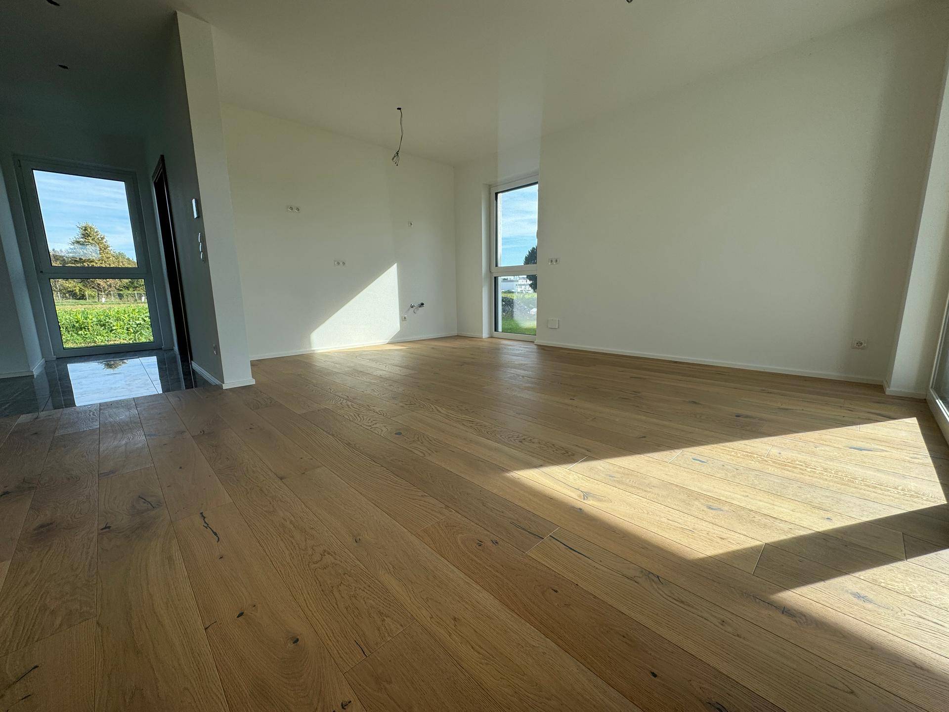 Lichtdurchflutetes Wohnzimmer mit hellem Eichenparkett und großen Fenstern.