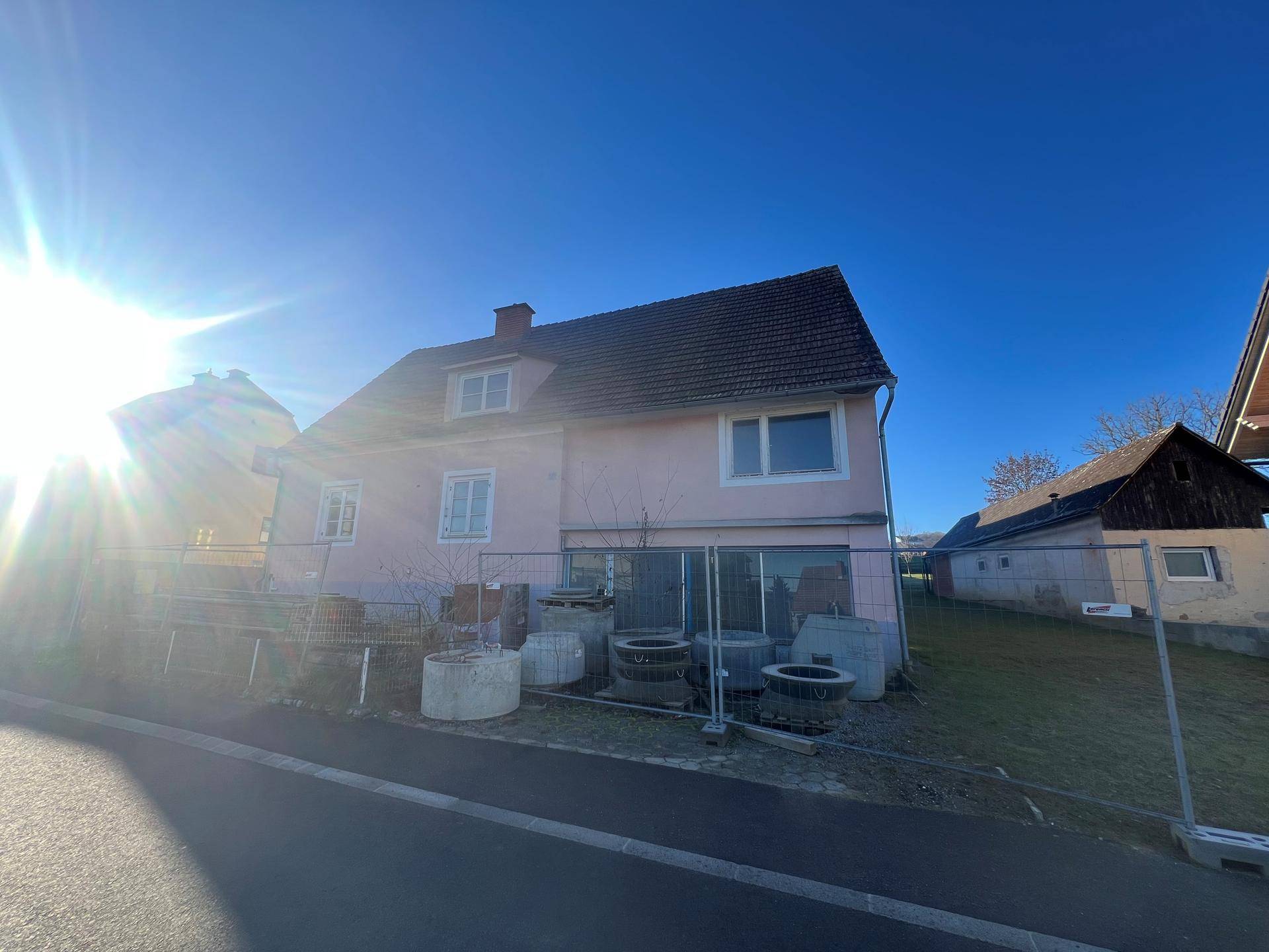 Sonnige Ansicht des rosa Hauses mit Bauzaun und Baumaterialien im Vordergrund.