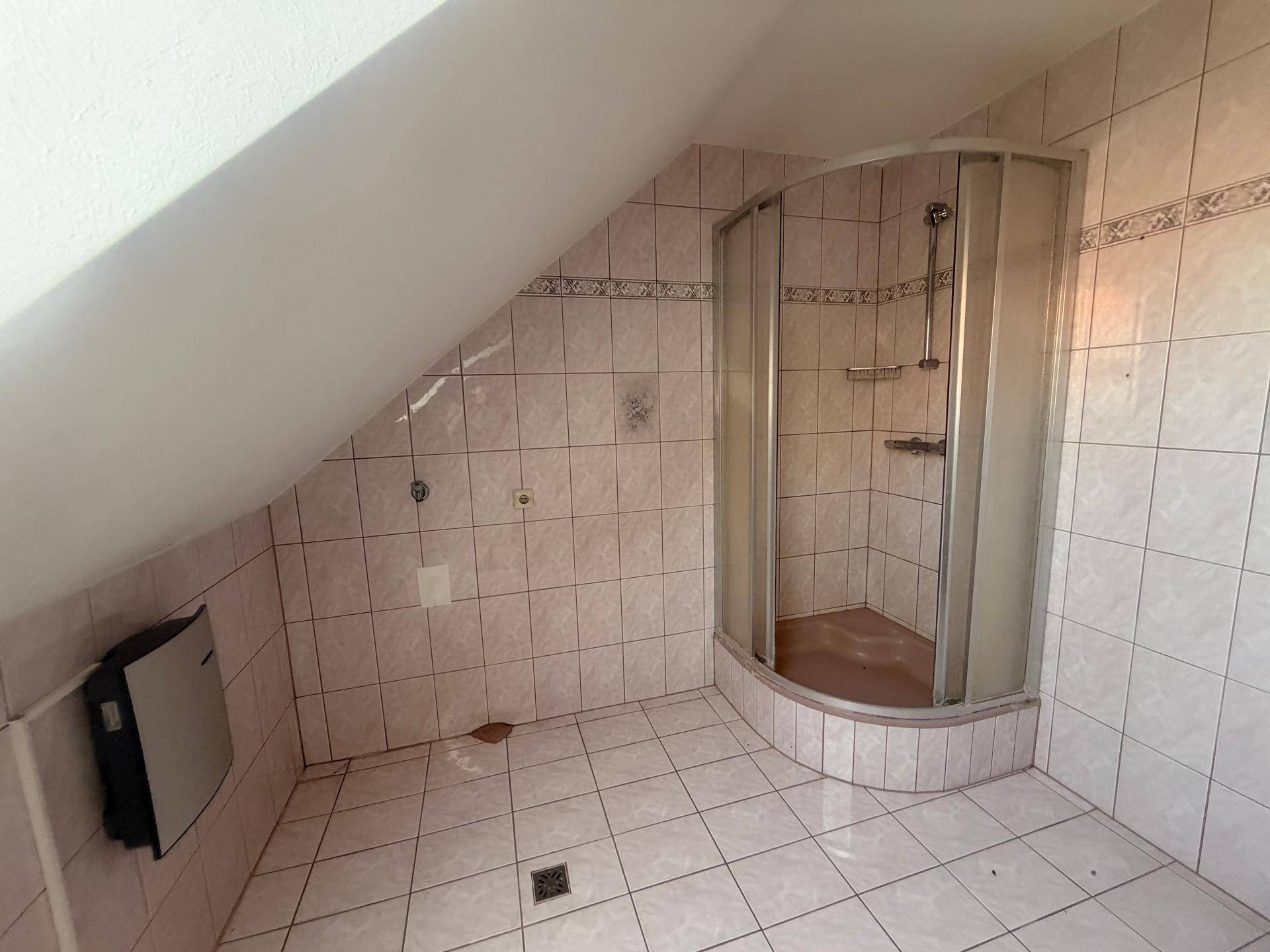 Badezimmer mit Duschkabine, rosa Fliesen, Dachschräge und Heizkörper in einfacher Ausstattung.