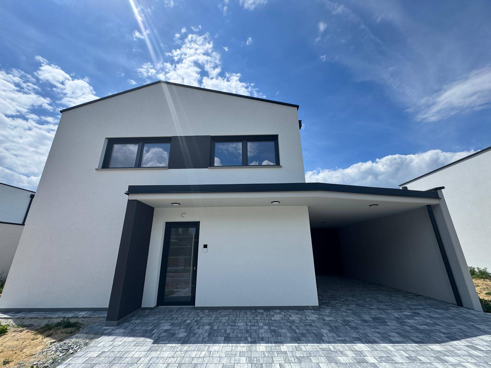 Moderne Hausfassade in Weiß mit dunklen Fensterrahmen und integriertem Carport.