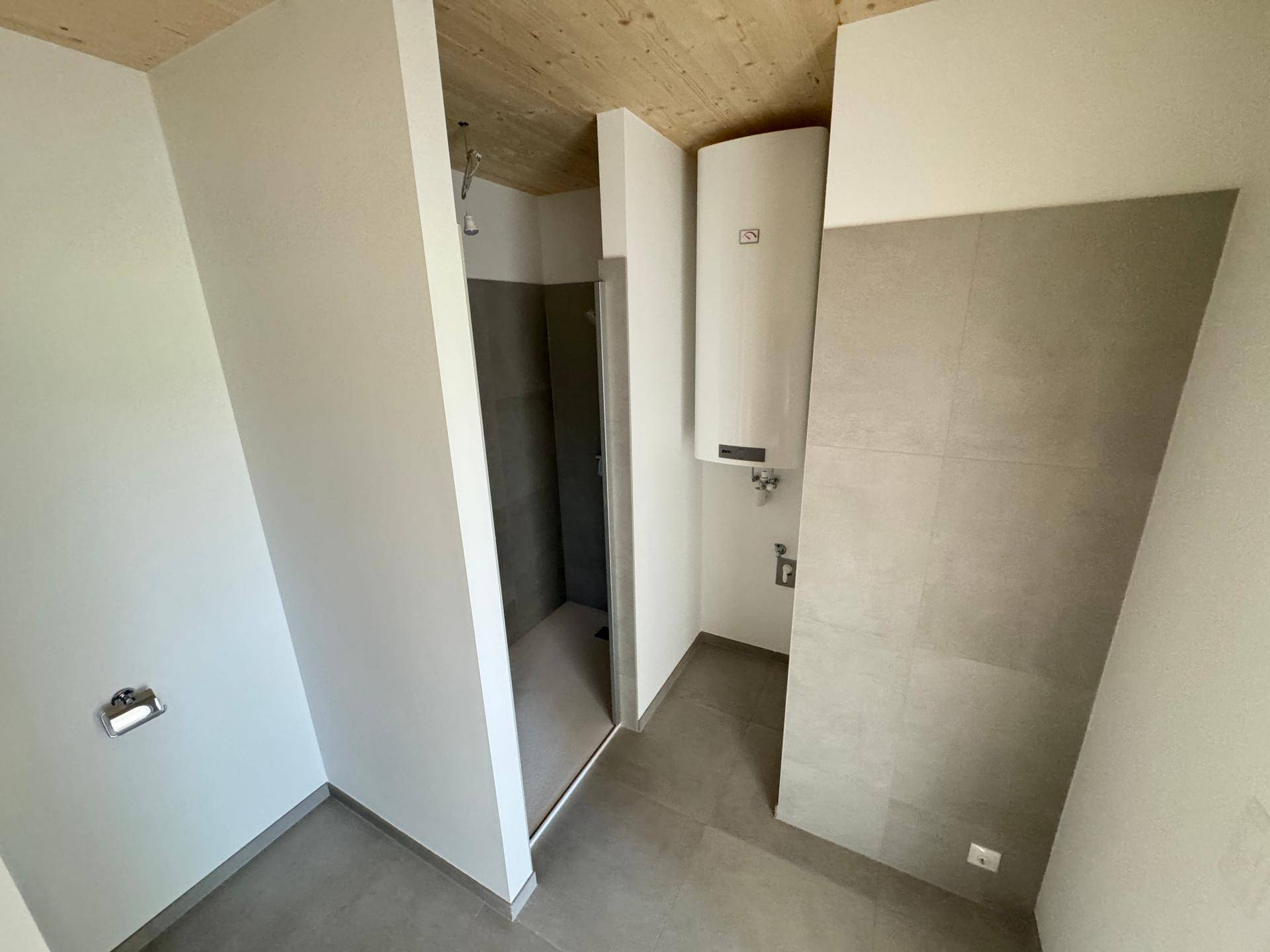 Modernes Badezimmer mit Duschbereich, Boiler und hellen Fliesen in einem Neubau.