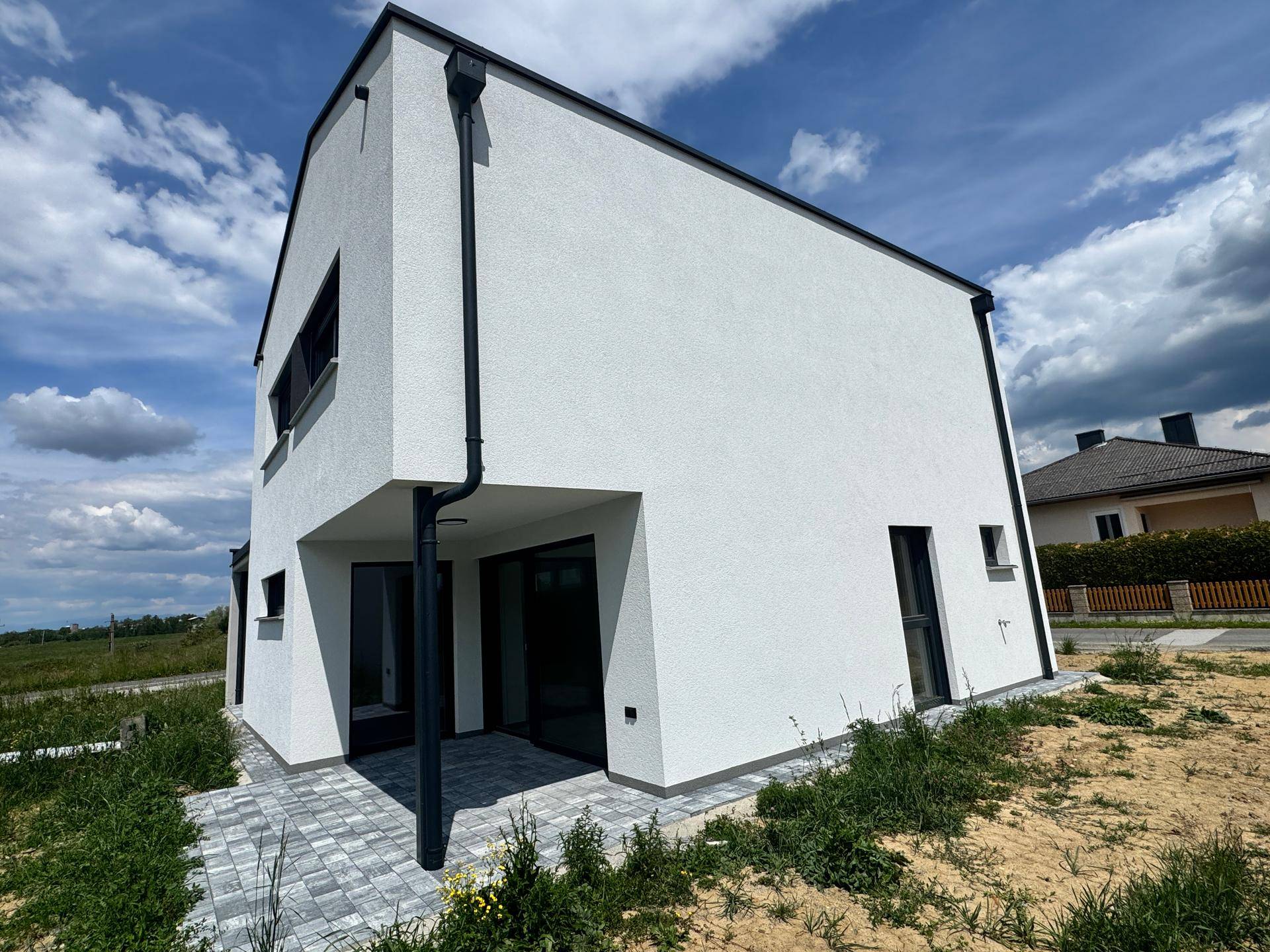 Seitenansicht des modernen Hauses mit kleiner gepflasterter Terrasse und Blick ins Grüne.