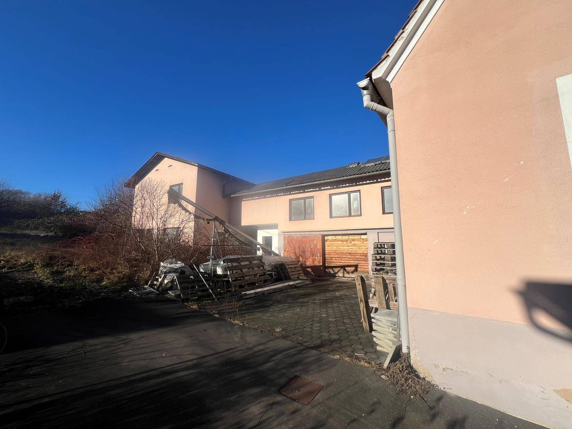 Hinterhofbereich mit gepflasterter Fläche, Garagen und Baumaterialien unter blauem Himmel.