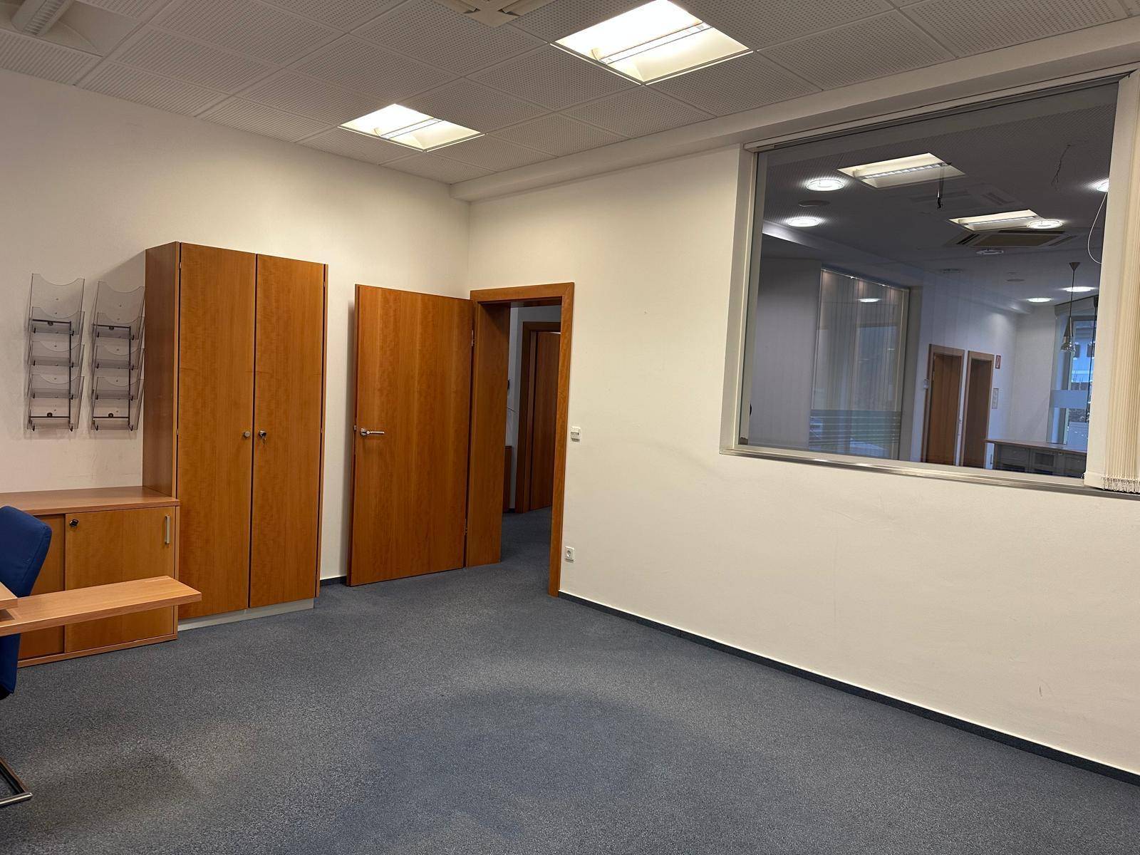 Geräumiges Büro mit Teppichboden, Einbauschränken und Blick in den Flur.