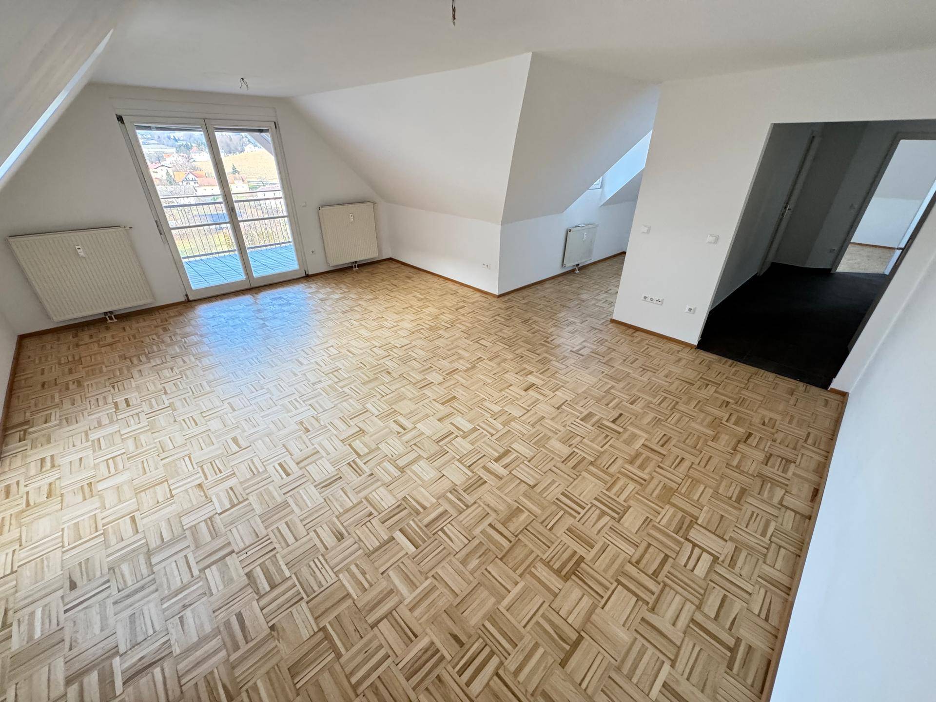 Geräumiges Zimmer im Dachgeschoss mit Parkettboden, Dachschrägen und Balkonzugang.
