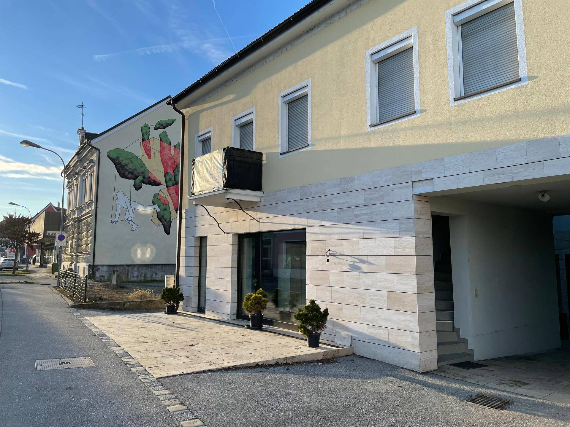 Ansicht des Gebäudes von der Seite mit einer modernen Fassade und einem Wandgemälde am Nachbargebäude.