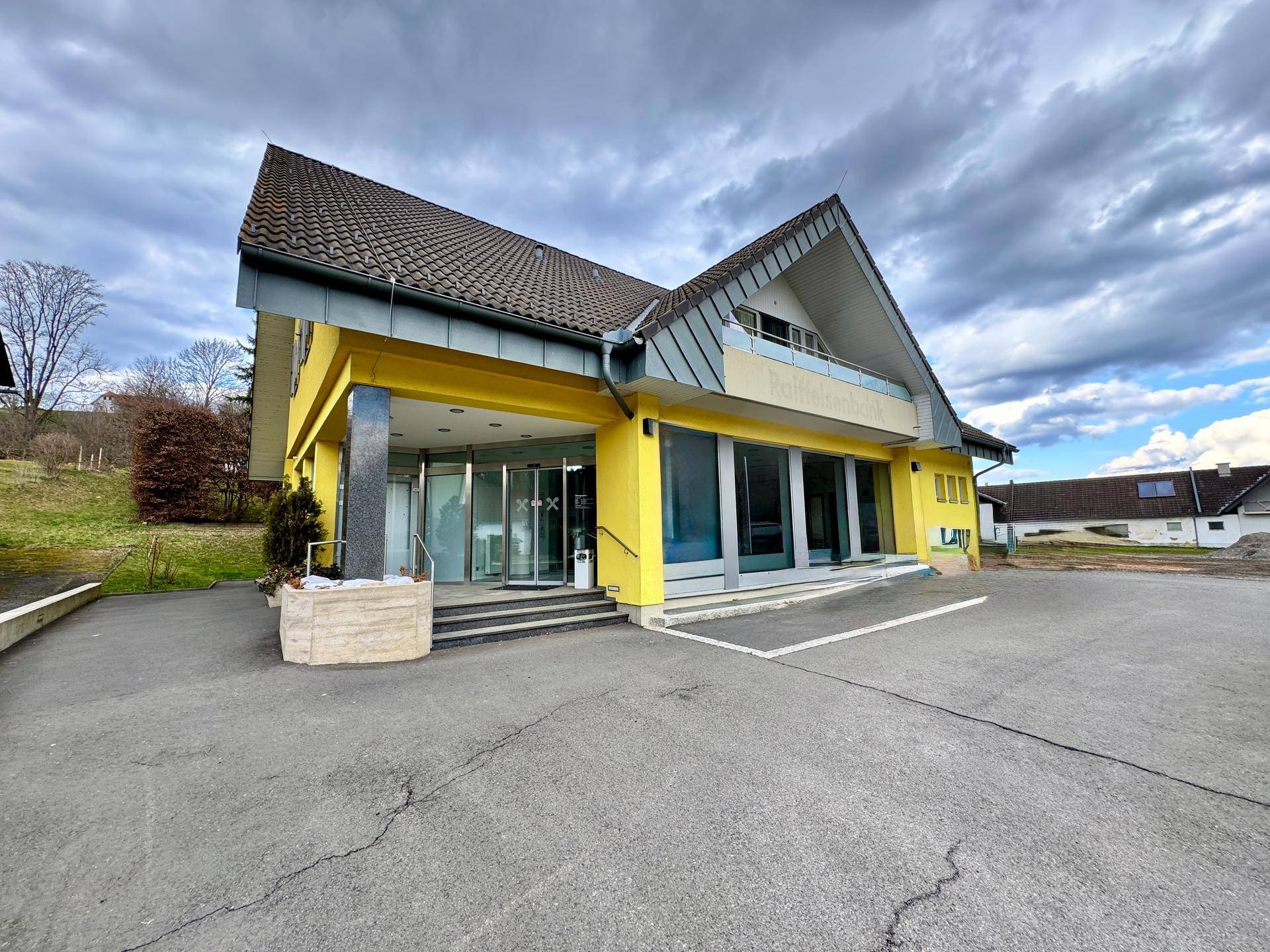 Breitere Ansicht des Eingangsbereichs mit Rampe und Stufen zum gelben Gebäude.