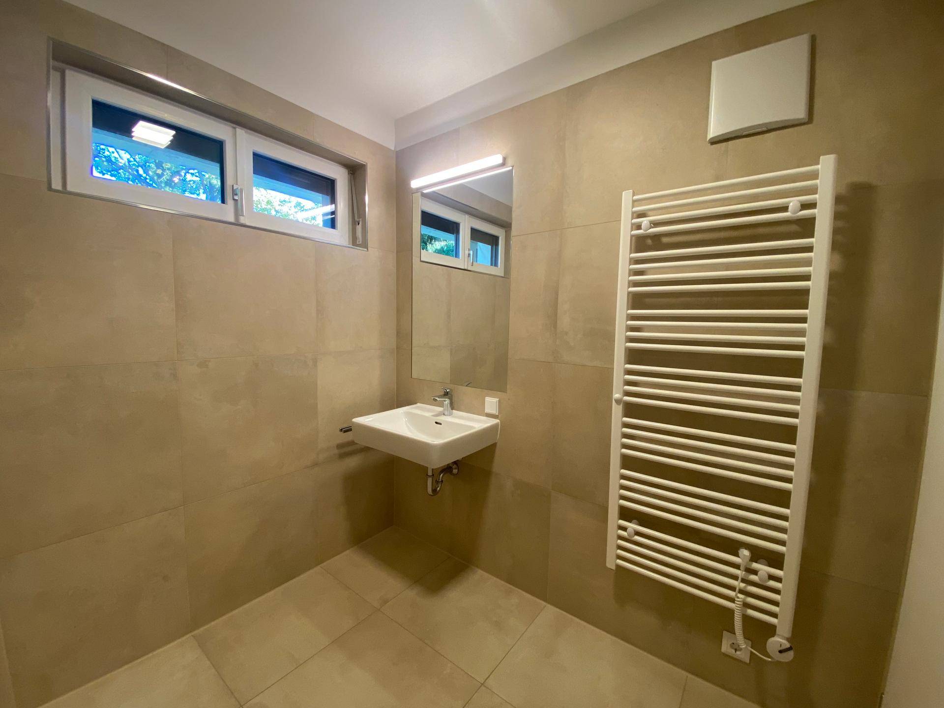 Modernes Badezimmer mit beigefarbenen Fliesen, Waschbecken, Spiegel und beheiztem Handtuchhalter.
