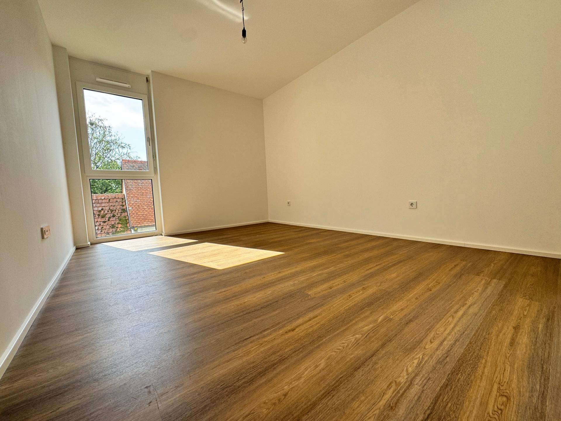 Helles Schlafzimmer mit Laminatboden und einem großen Fenster, das viel Tageslicht hereinlässt.