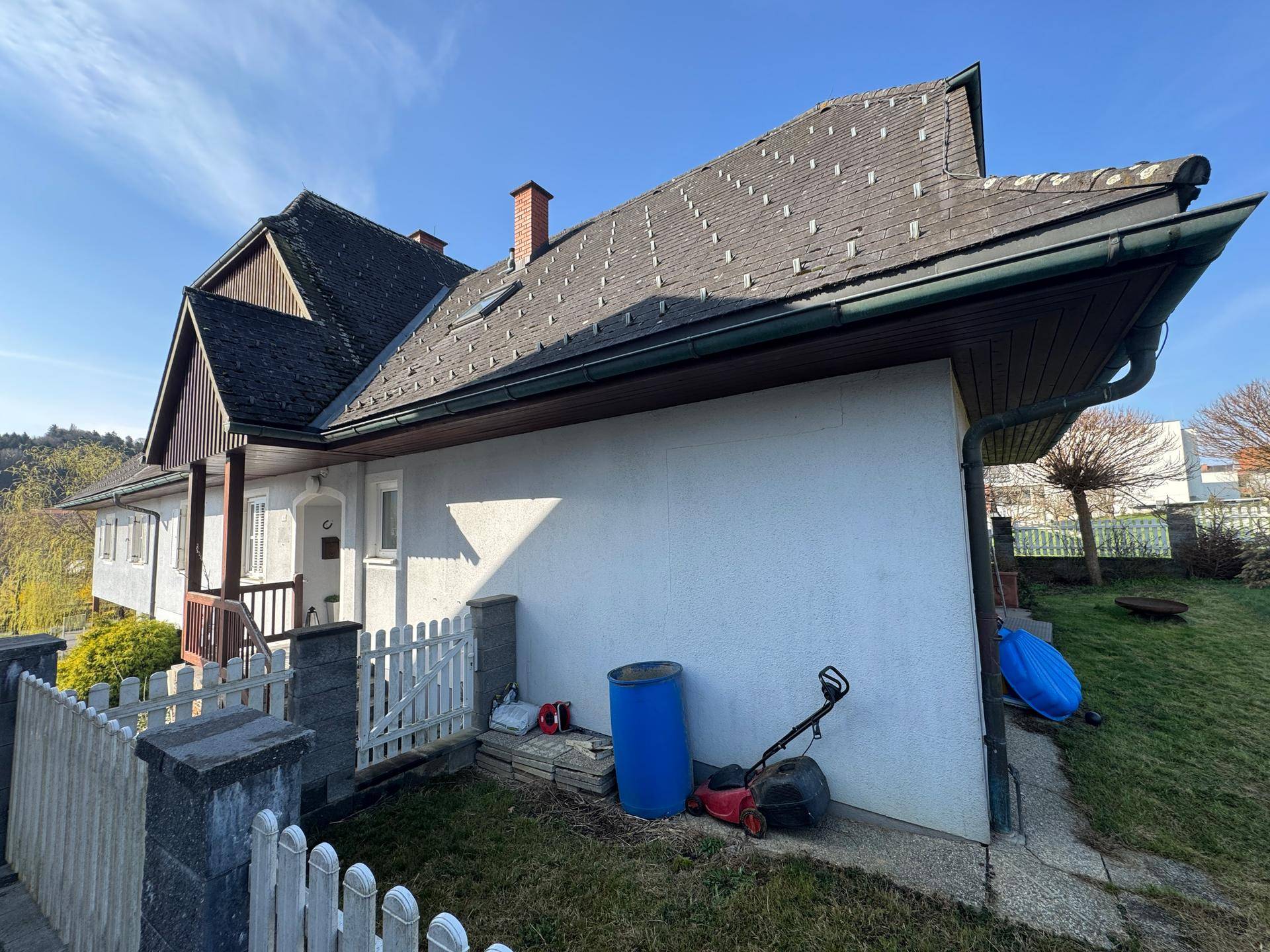 Seitenansicht des Hauses mit kleinem Eingangsbereich und weißem Lattenzaun im Vorgarten.