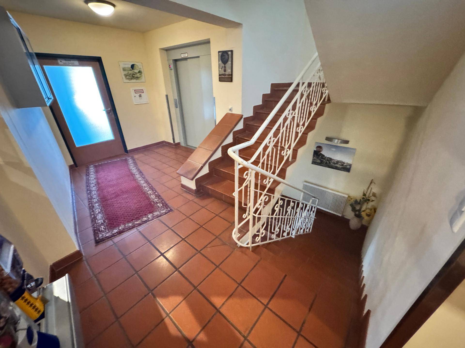 Treppenhaus mit Fliesenboden, Aufzug und Teppichläufer.