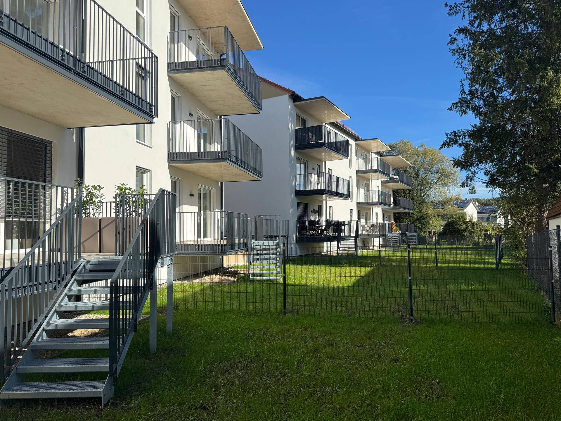 Rückseite eines modernen Wohngebäudes mit mehreren Balkonen und einer weitläufigen Rasenfläche.