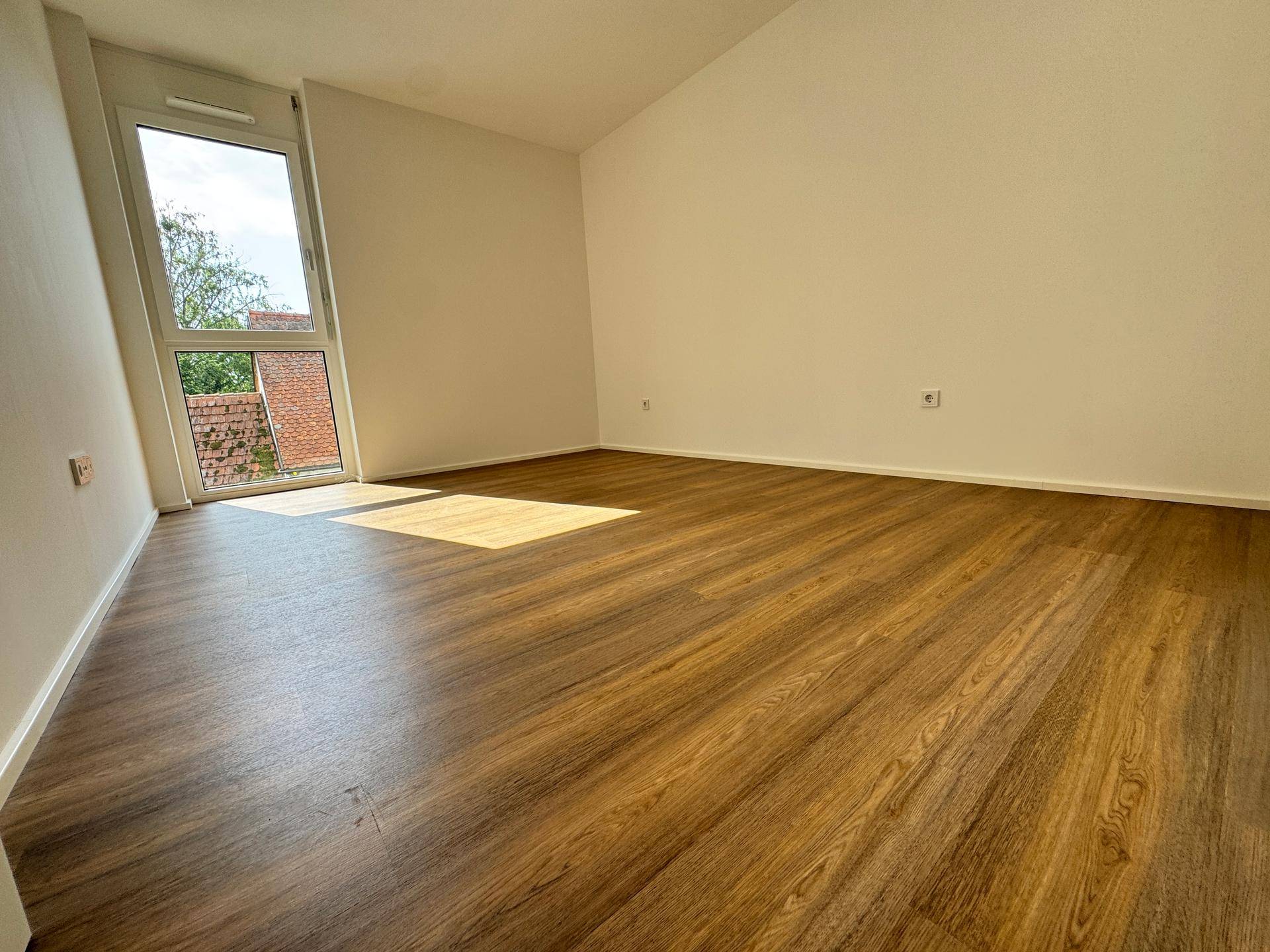 Geräumiges Schlafzimmer mit Holzboden und schrägem Fenster, das viel Sonnenlicht bietet.