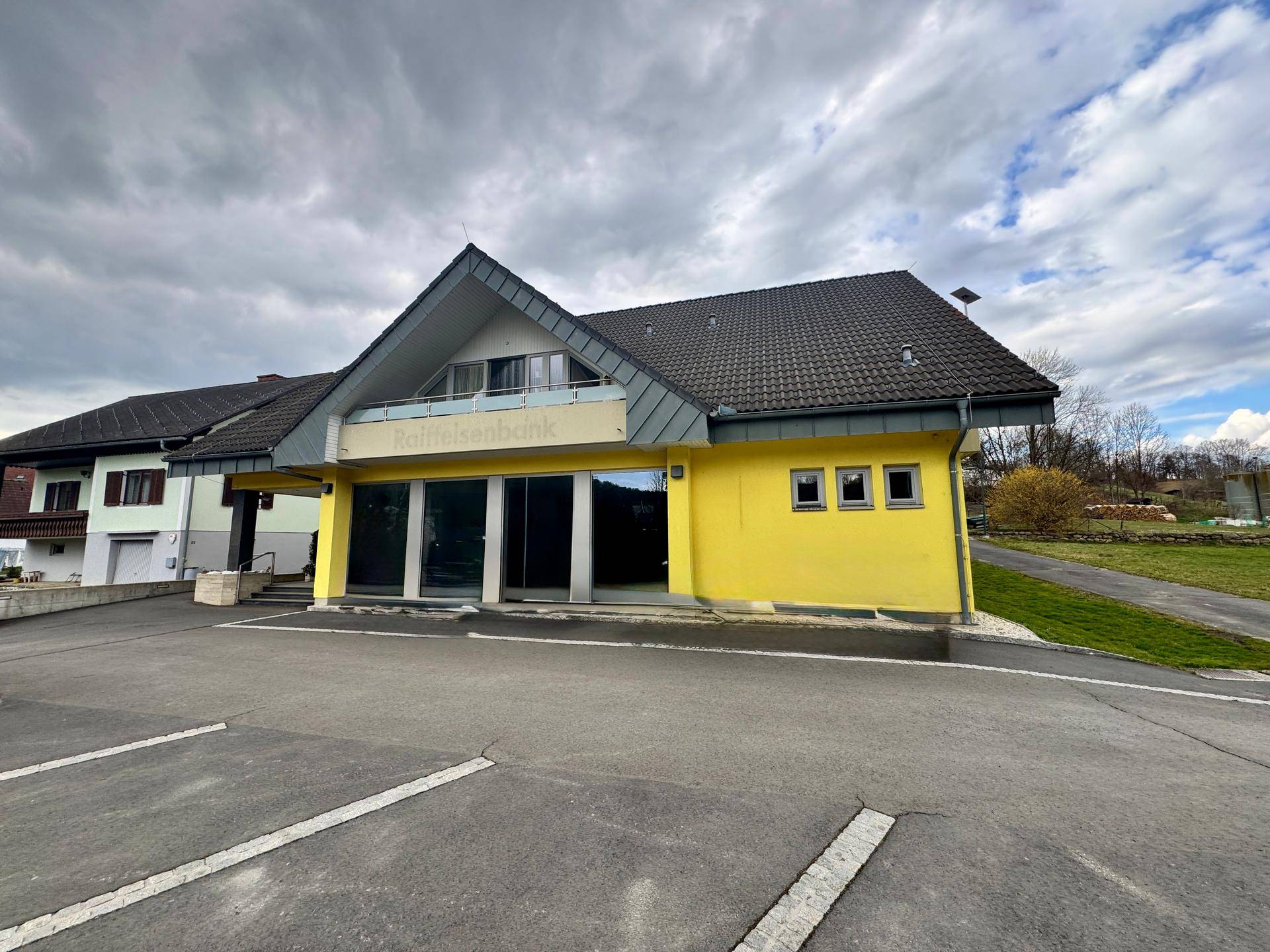 Ansicht des gelben Gebäudes mit Parkplatz und umliegender grüner Landschaft.