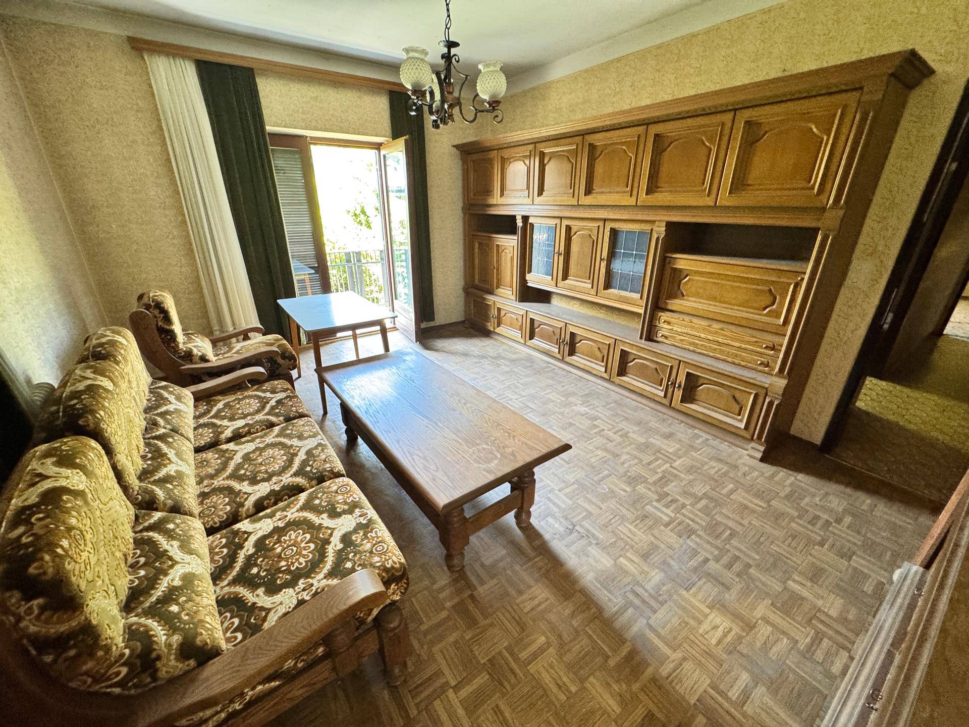 Wohnzimmer mit großer Holzschrankwand, traditionellen Sitzmöbeln und Balkonzugang.