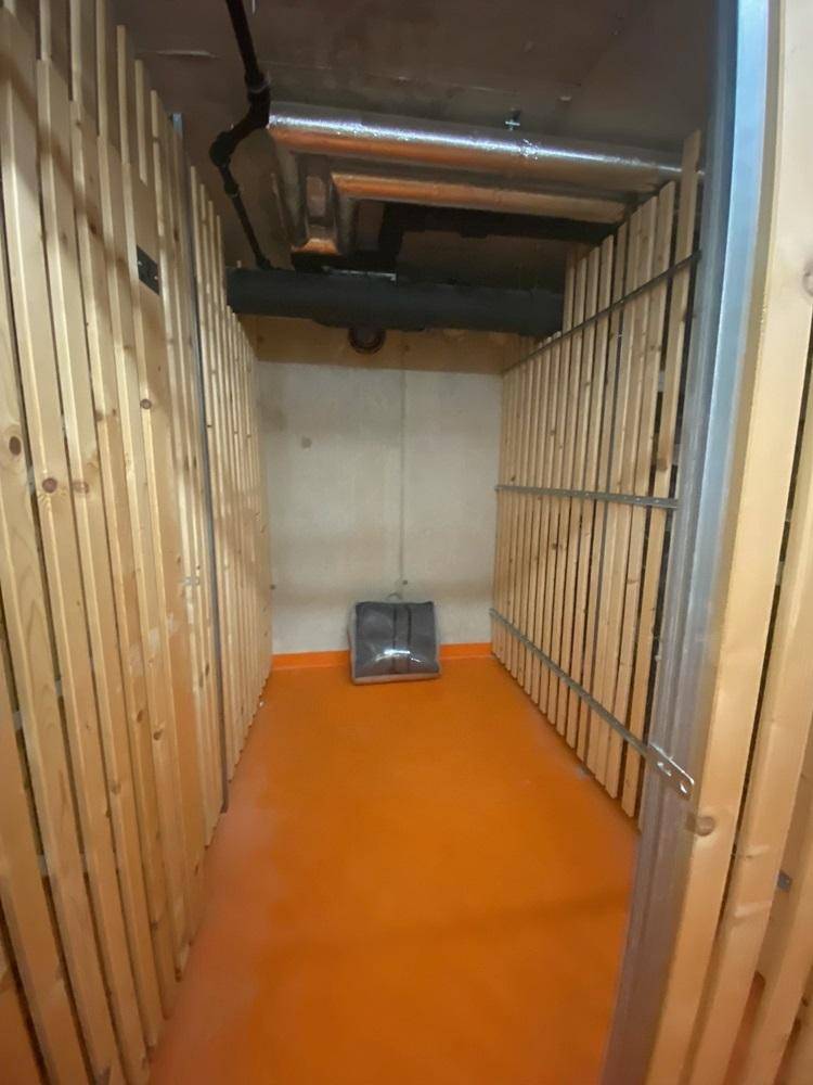 Kellerabteil mit Holzlattenwänden und orangefarbenem Boden für zusätzlichen Stauraum.