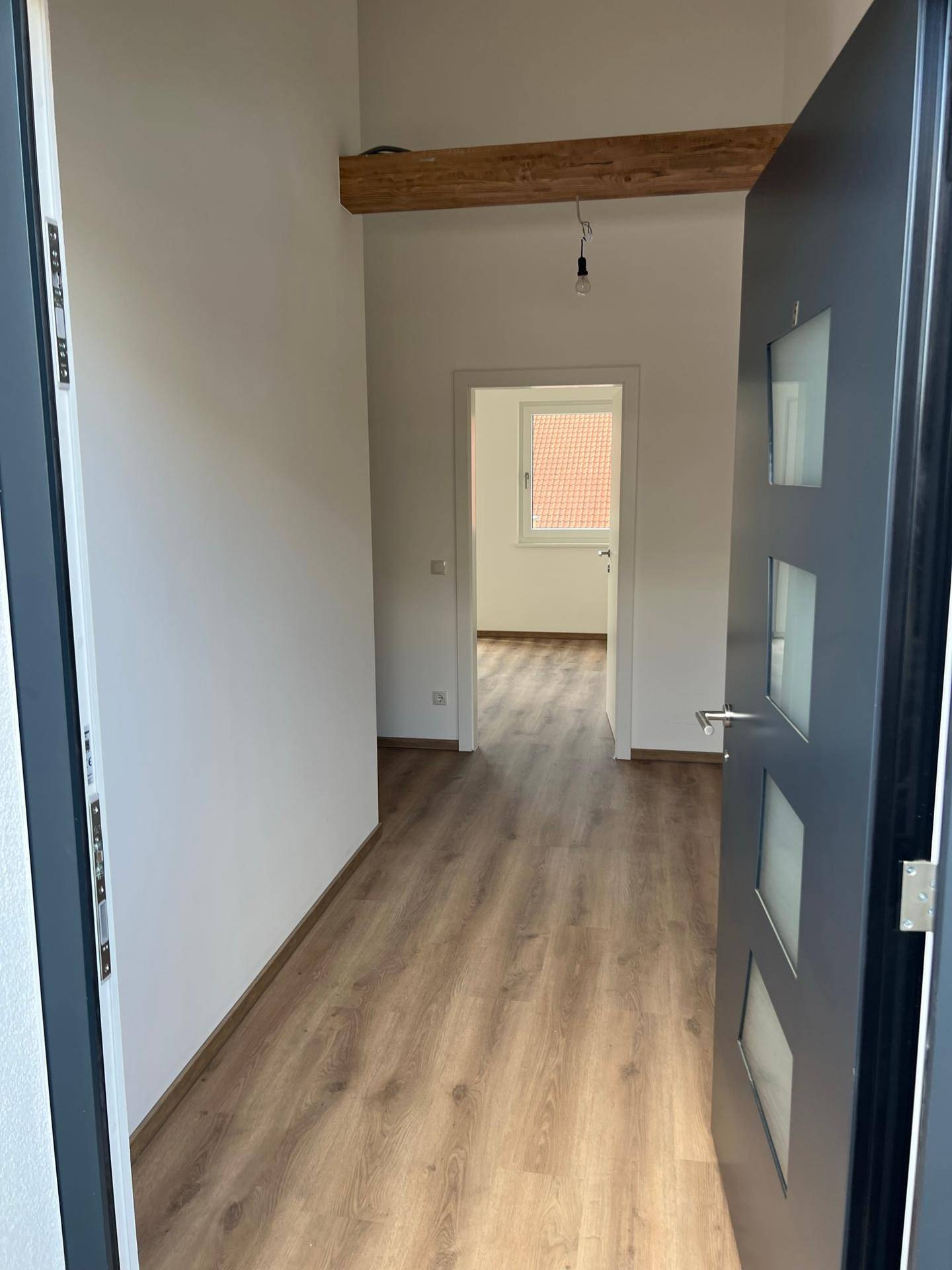 Heller Flur mit Laminatboden und Blick in ein weiteres Zimmer mit Fenster und Holzbalken.