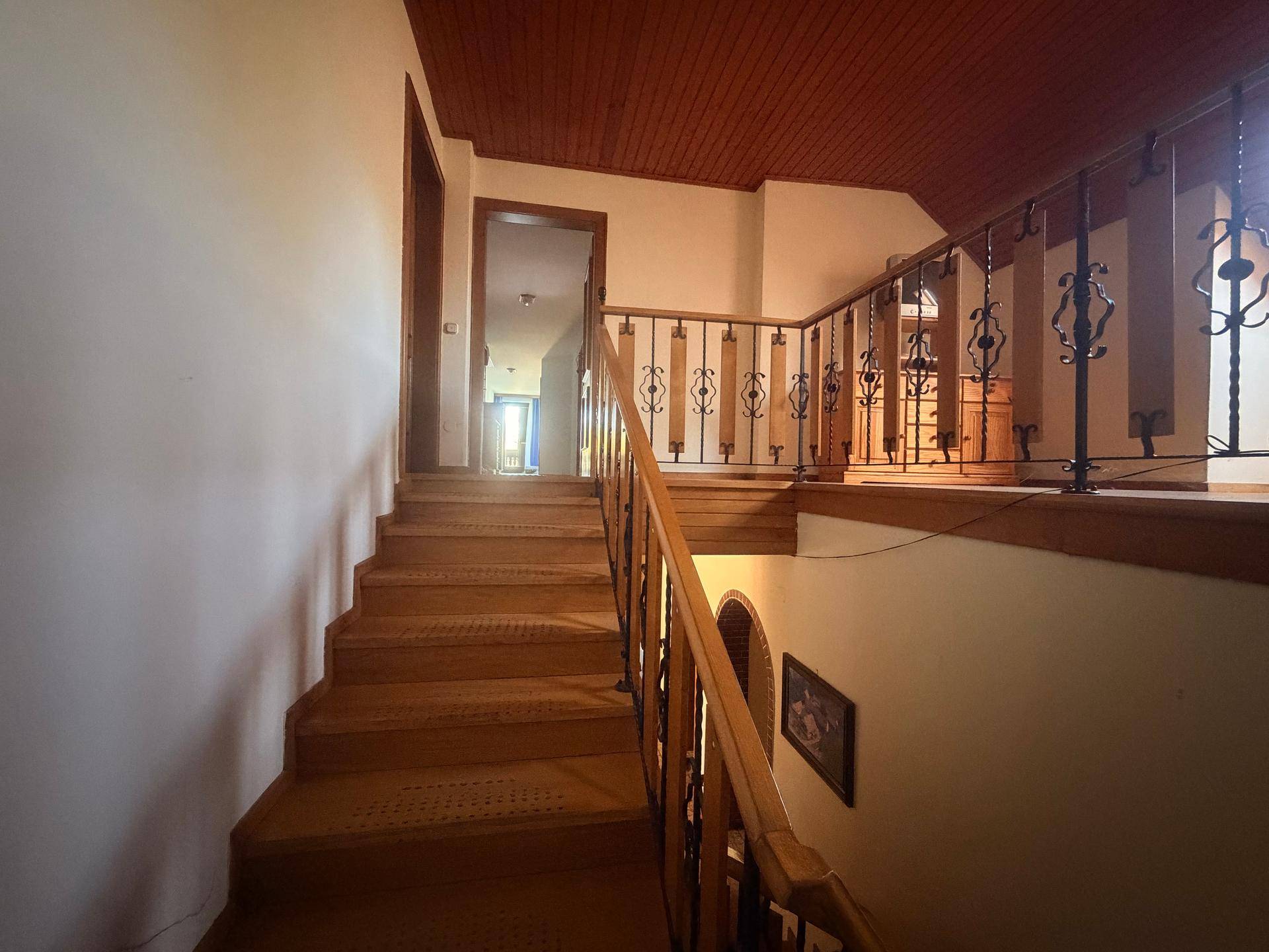 Holztreppe führt in den oberen Stock, mit Holzdecke und schmiedeeisernem Geländer.