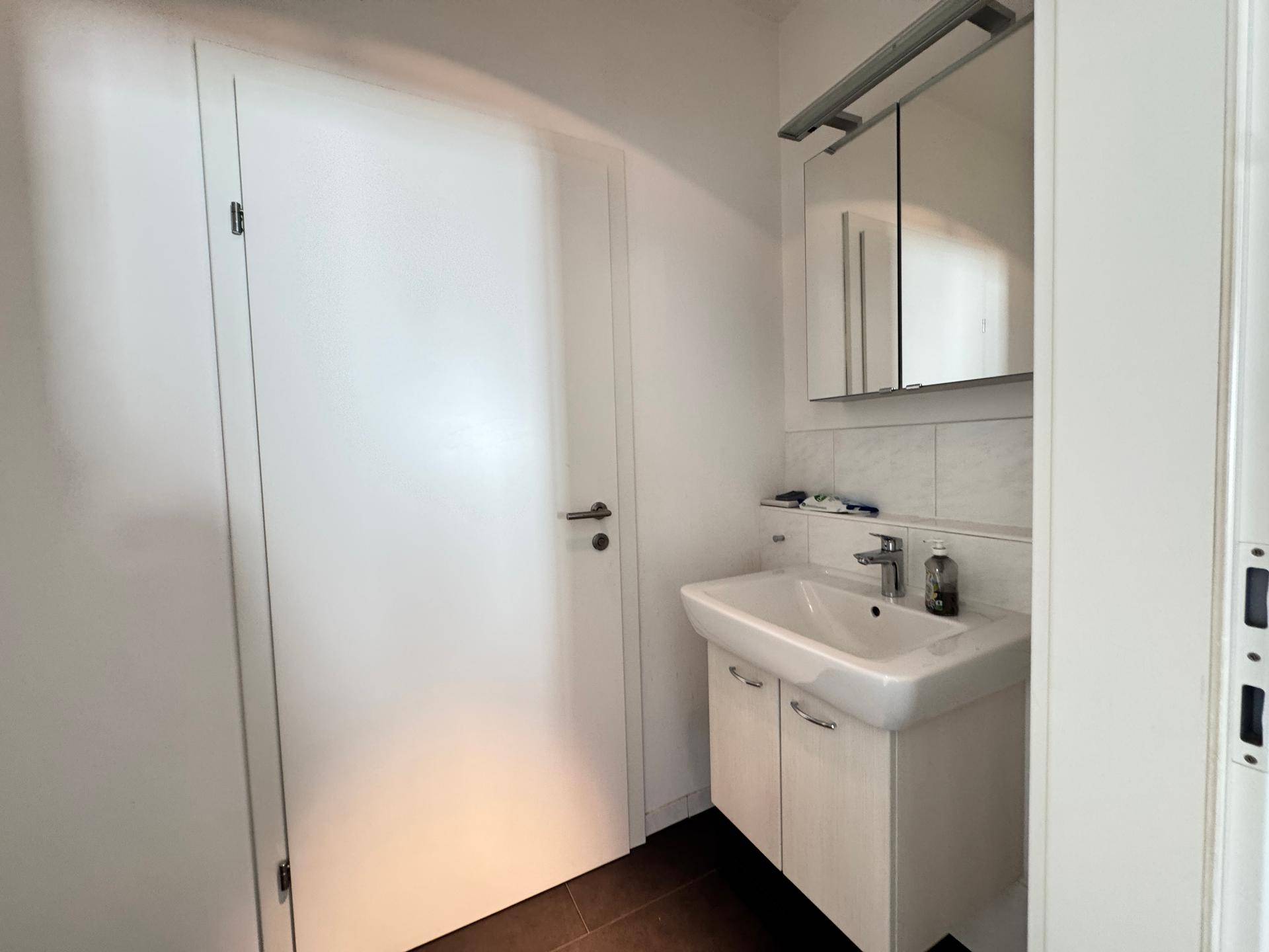 Kleines Gäste-WC mit Waschbecken, Spiegelschrank und weißen Wandfliesen.